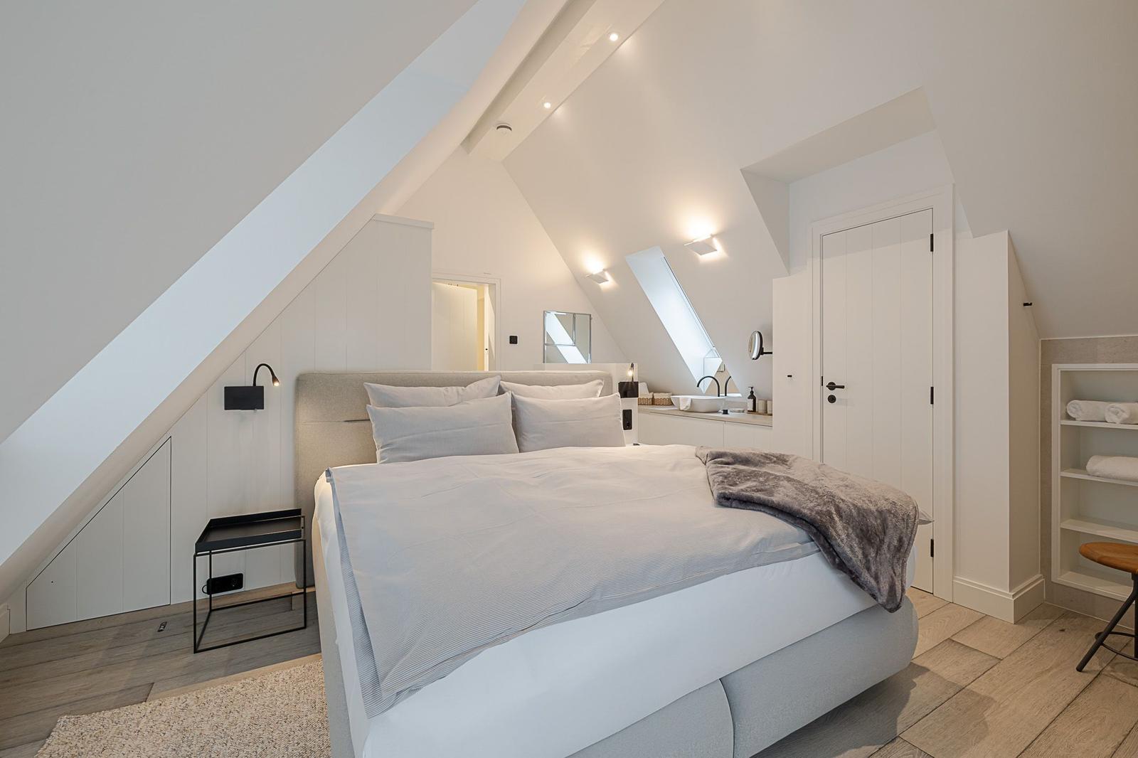 Schlafzimmer mit Dachschrägen, Bett, Nachttisch und Badebereich.