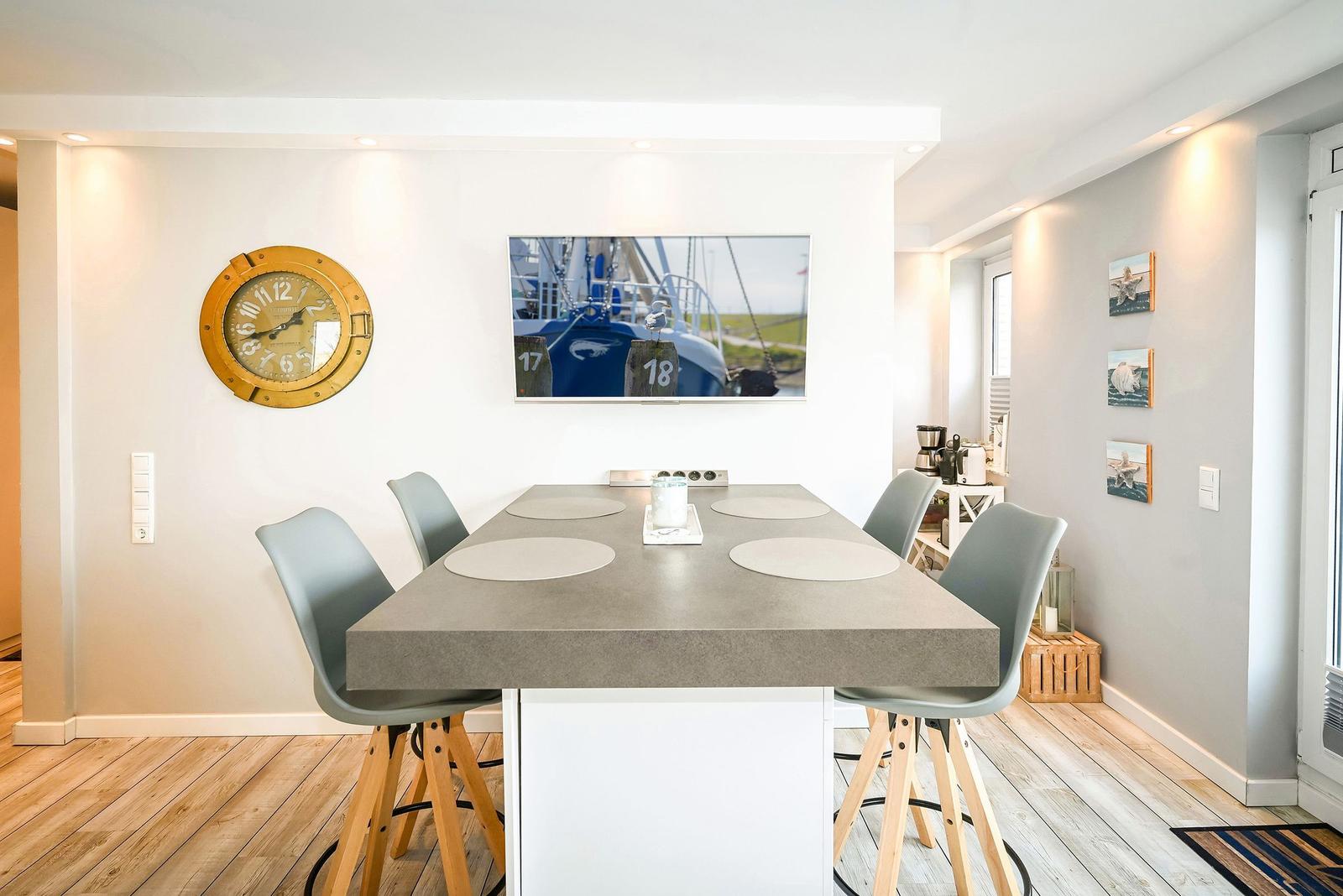 Essbereich mit Tisch und Stühlen, Wanduhr und Bild an der Wand.