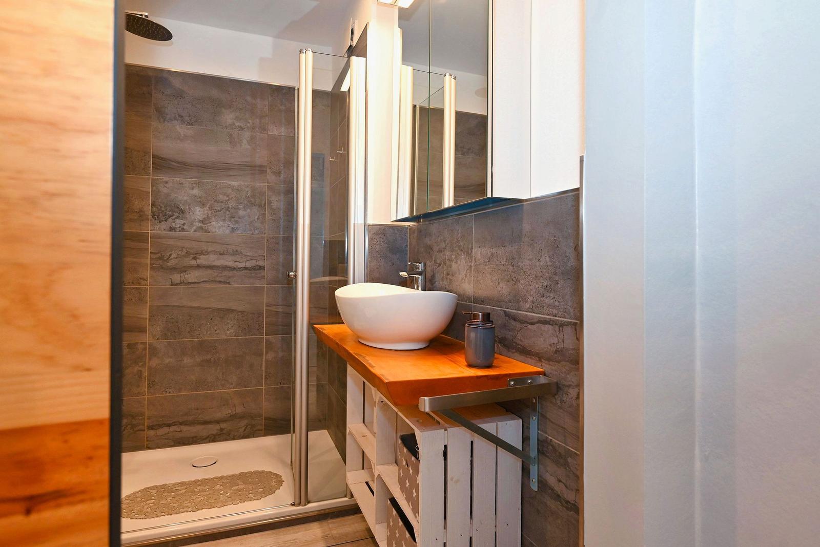 Dusche mit Glaswand, Waschbecken auf Holzplatte und Spiegelschrank