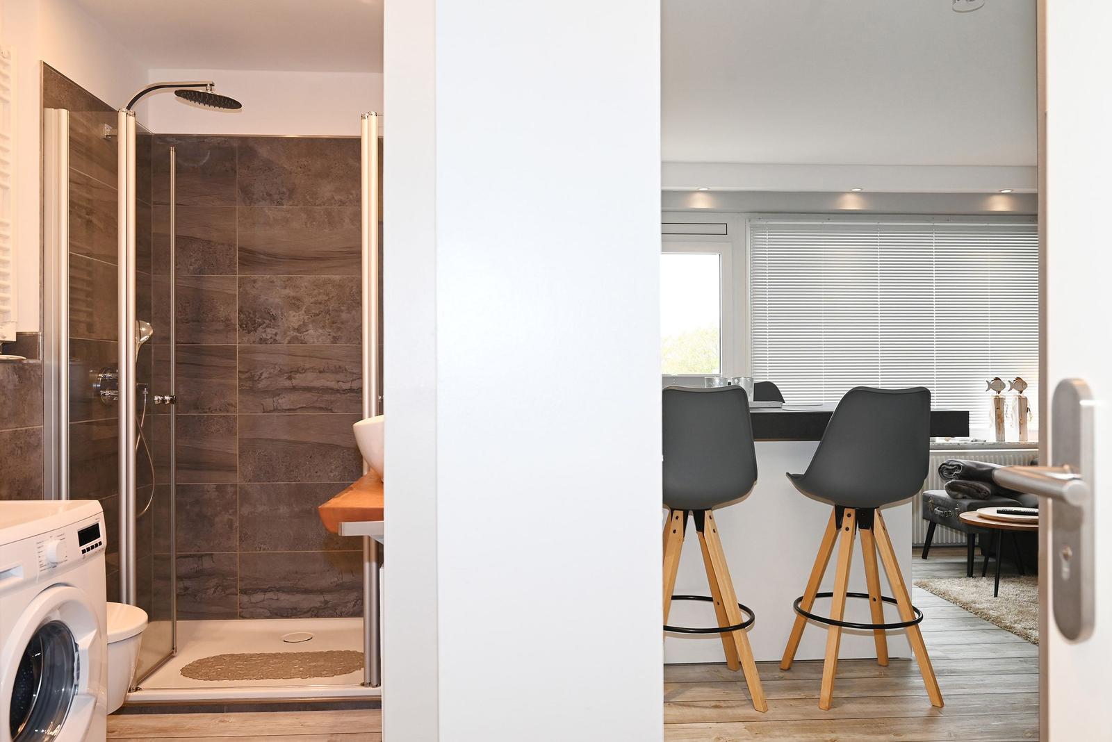 Bad mit Dusche und Waschmaschine. Küche mit Barhocker und Fenster.