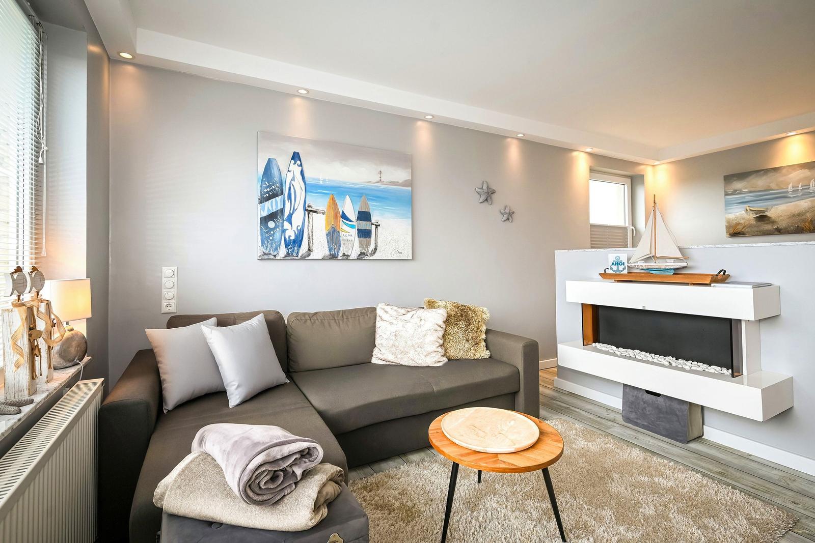 Wohnzimmer mit Sofa, Kamin und Wandbildern mit Surfbrettern und Segelbooten.