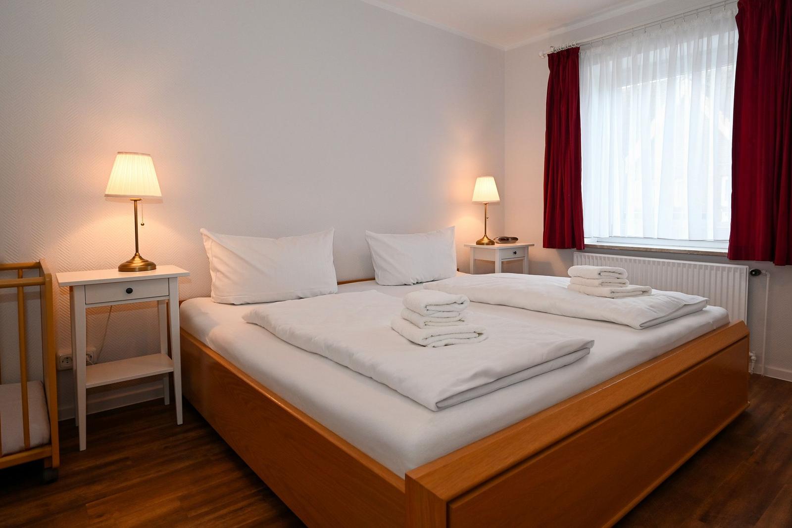 Ein Schlafzimmer mit Doppelbett, zwei Nachttischen und roten Vorhängen.