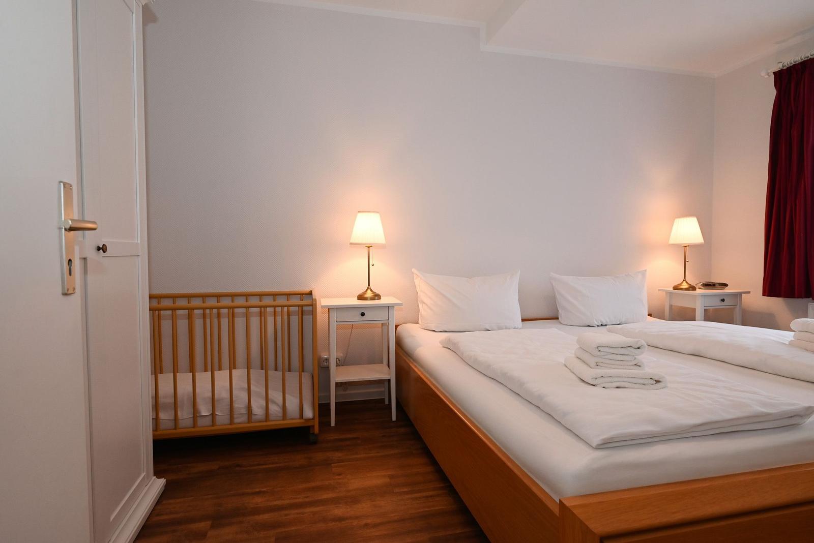 Schlafzimmer mit Bett, Kinderbett und zwei Nachttischen mit Lampen.