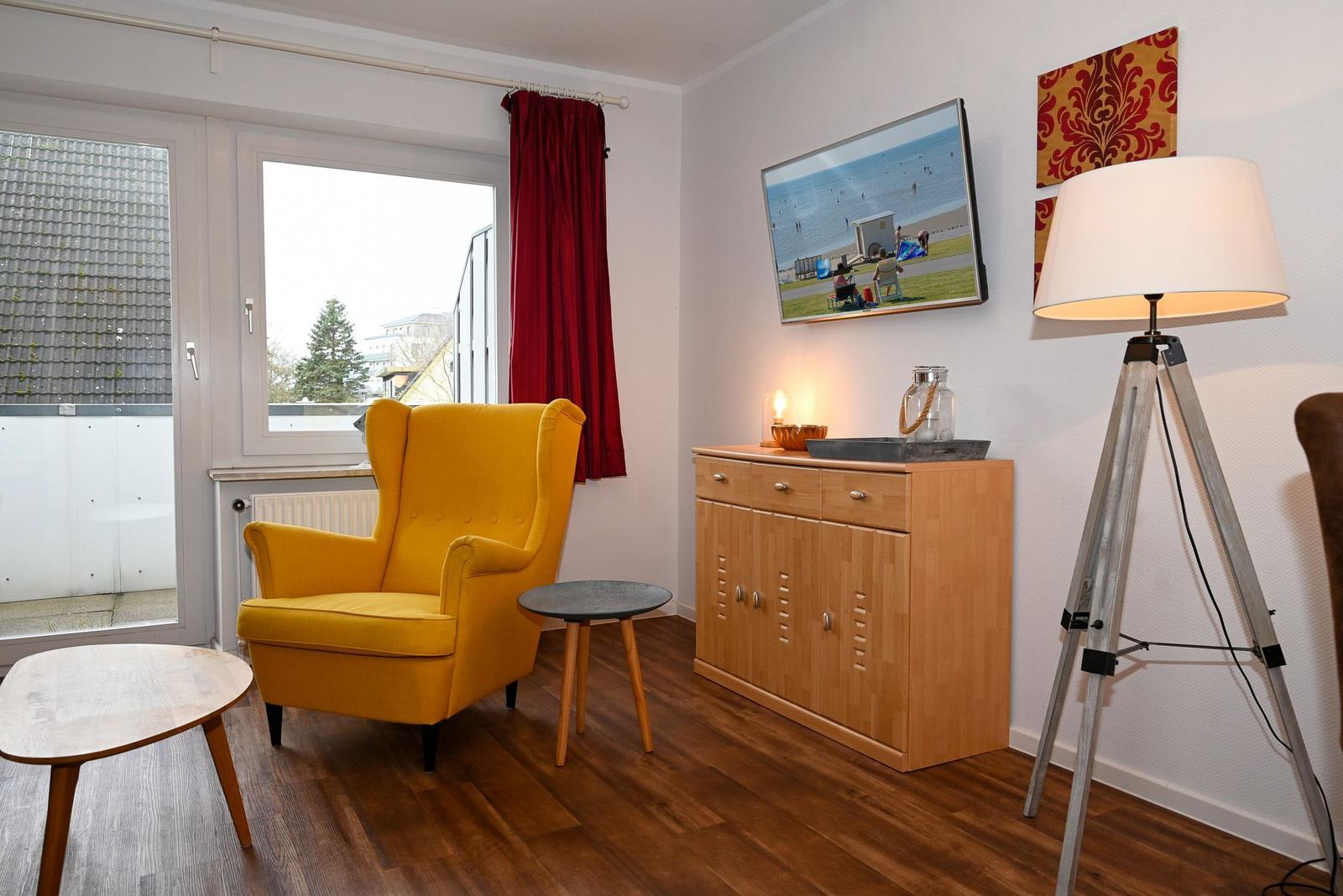 Ein Raum mit gelbem Sessel, Holzboden und TV an der Wand.