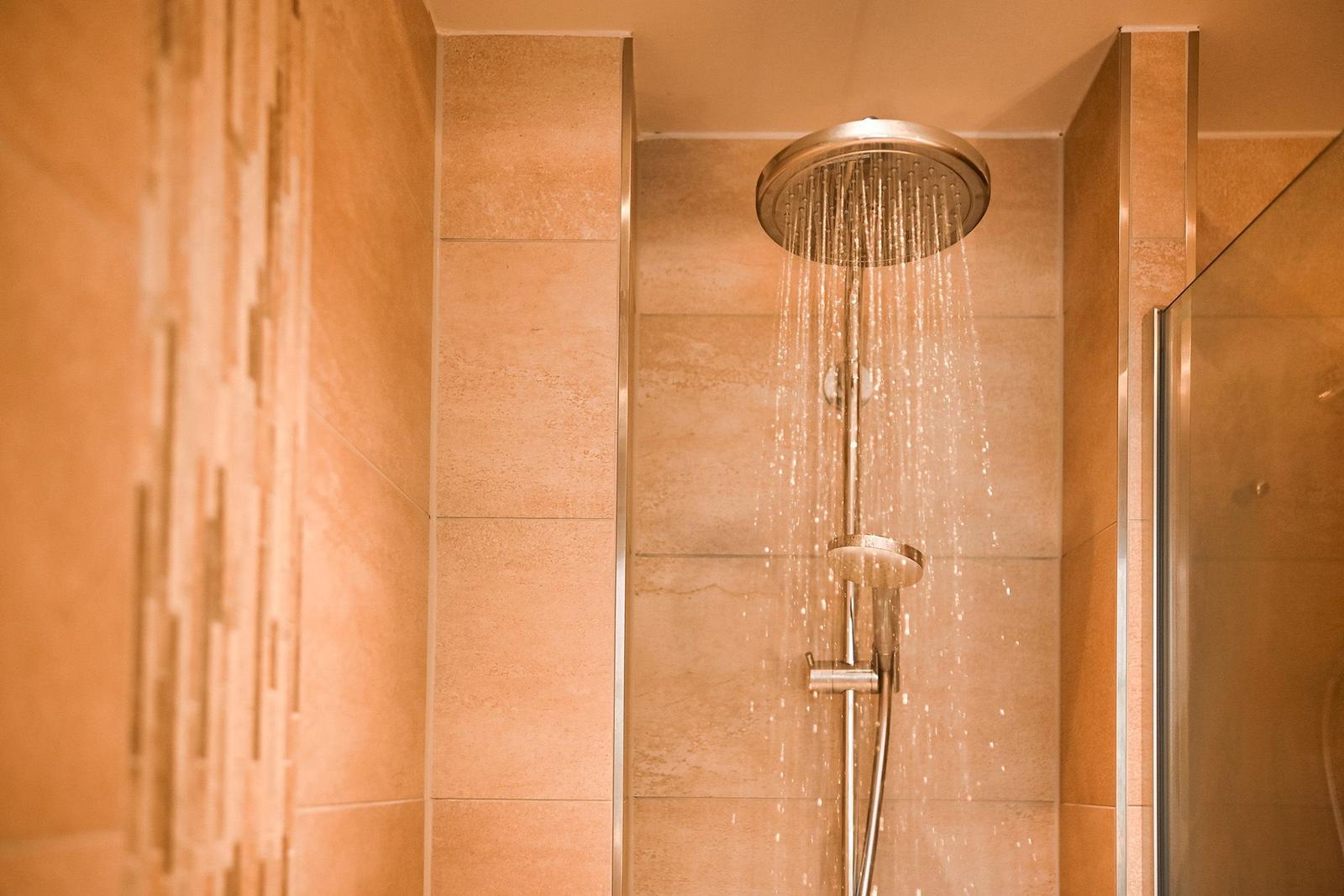 Dusche mit Regenduschkopf und Handbrause in Steinwandverkleidung.