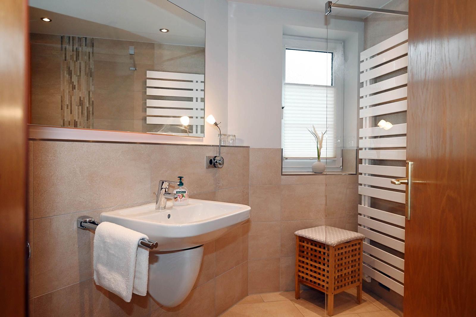 Badezimmer mit Waschbecken, Spiegel, Dusche und Heizkörper.