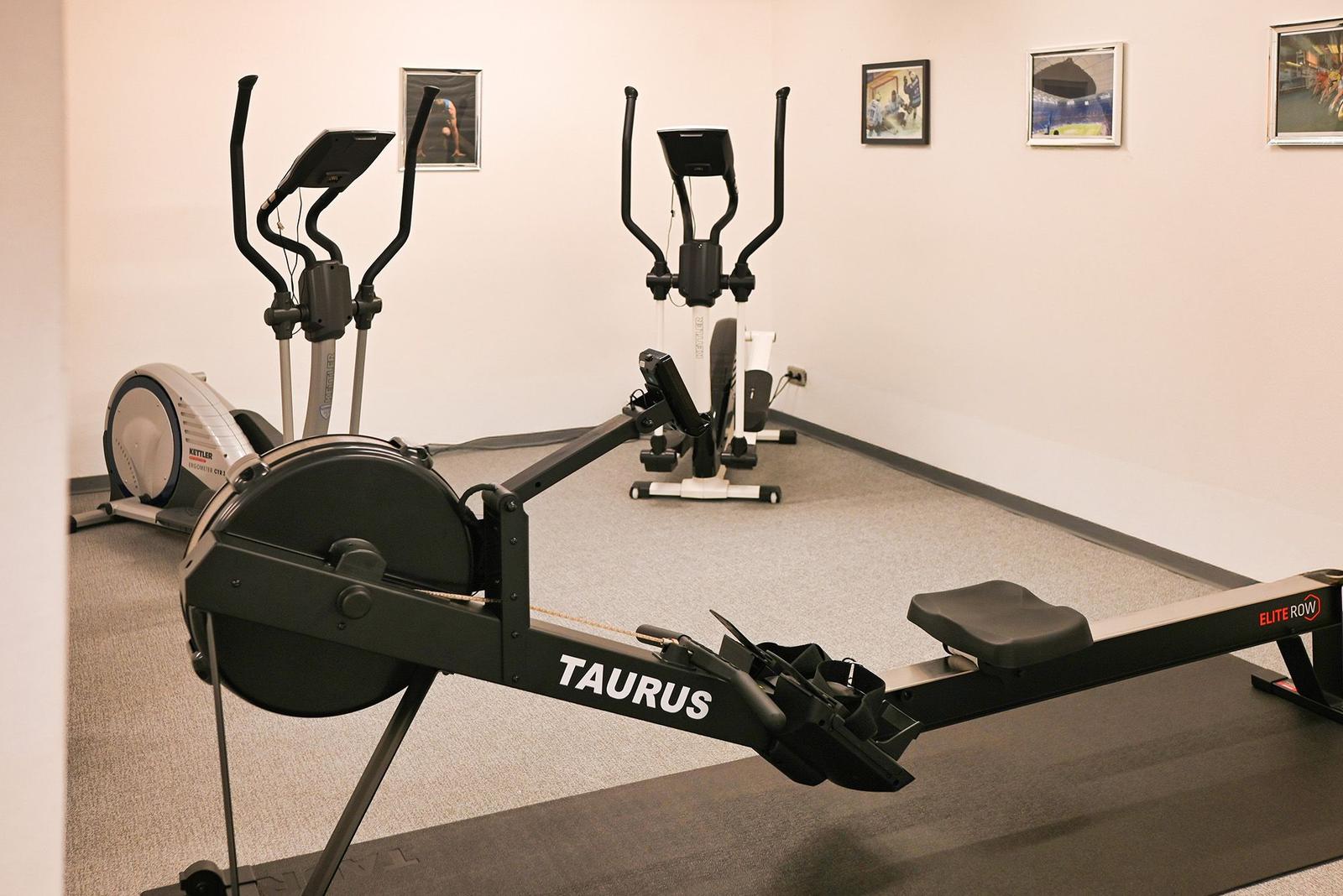 Fitnessraum mit Laufband und Rudergerät. Wandbilderrahmen an der Wand.