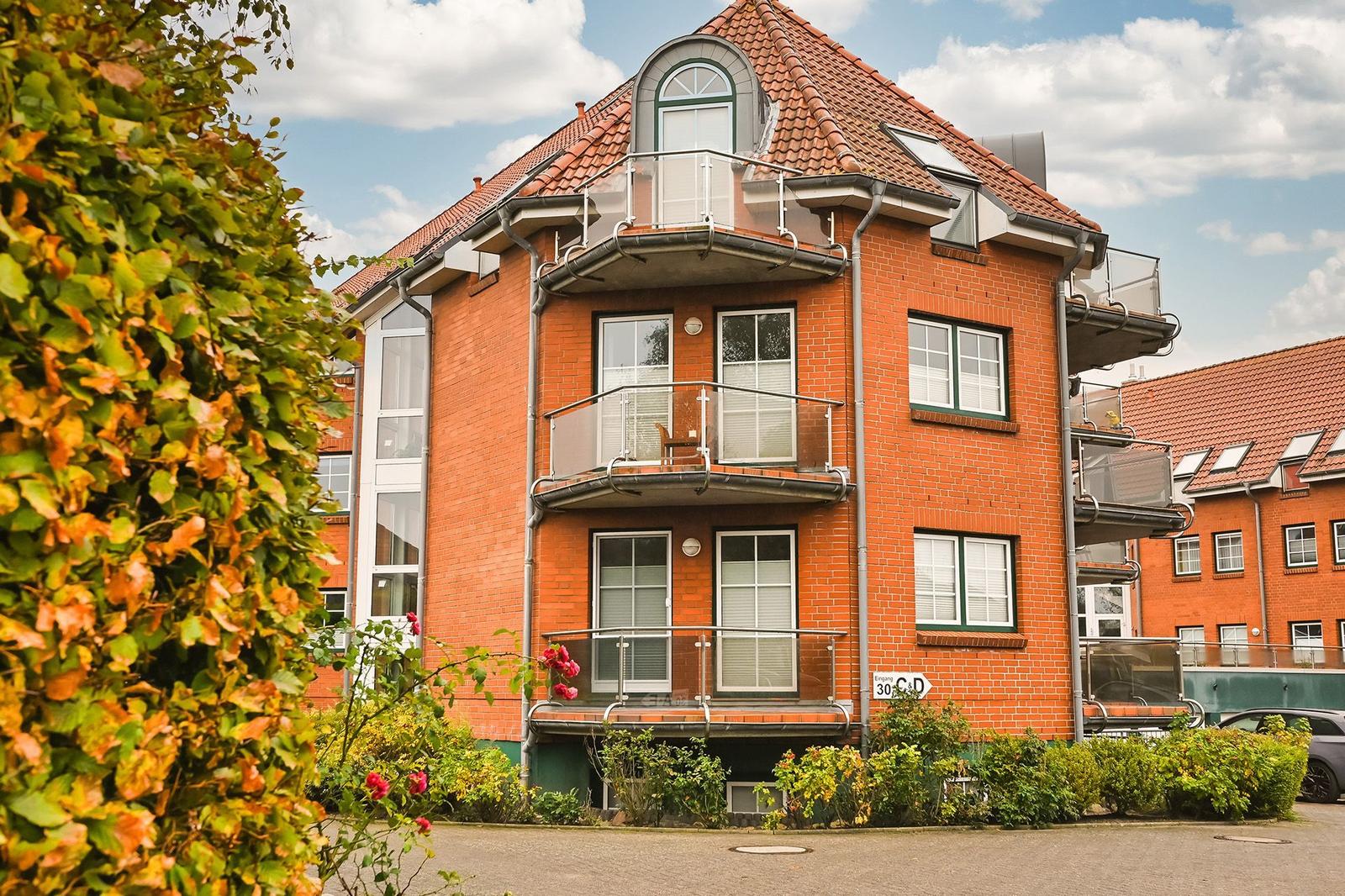 Rotes Backsteingebäude mit Balkonen und Dachfenstern, umgeben von Grünflächen.