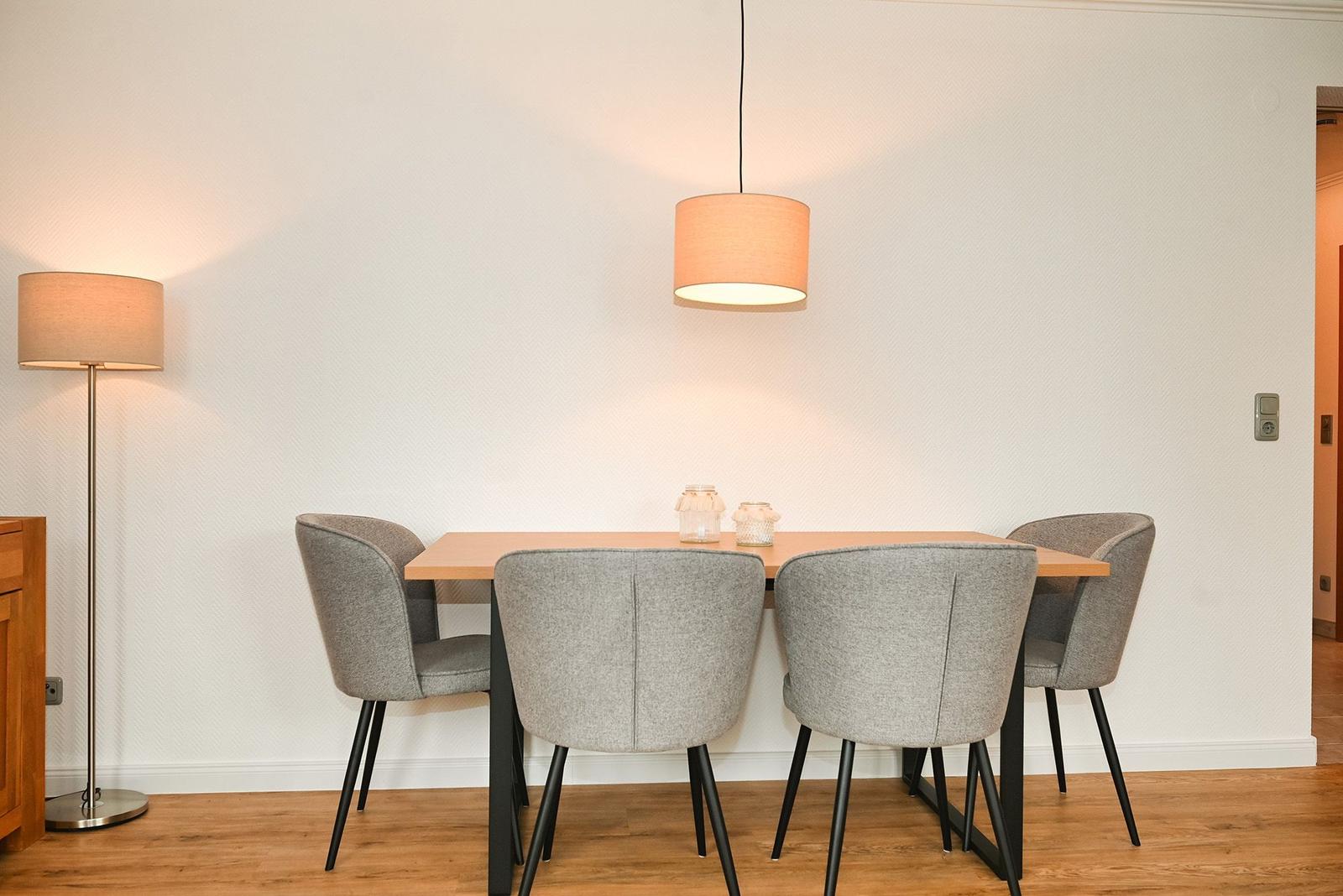 Esstisch mit vier Stühlen, Pendelleuchte und Stehlampe vor strukturiertem Wandbezug.