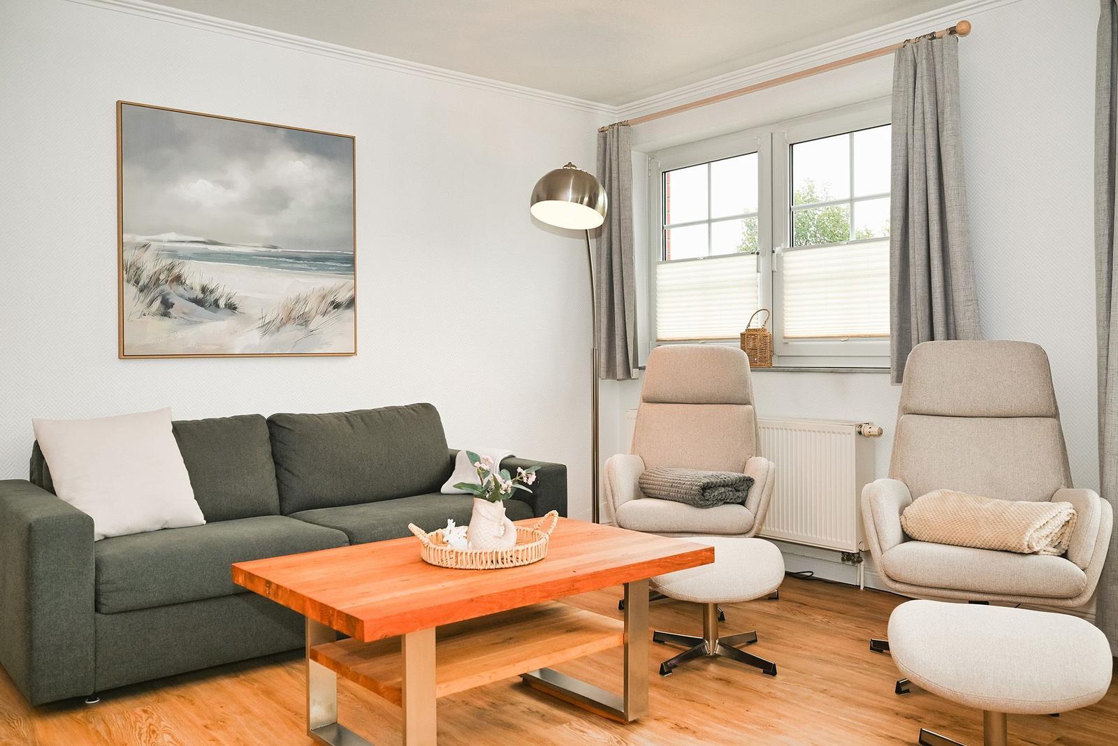 Ein Wohnzimmer mit Sofa, zwei Sesseln und einem Holztisch. An der Wand hängt ein Bild.