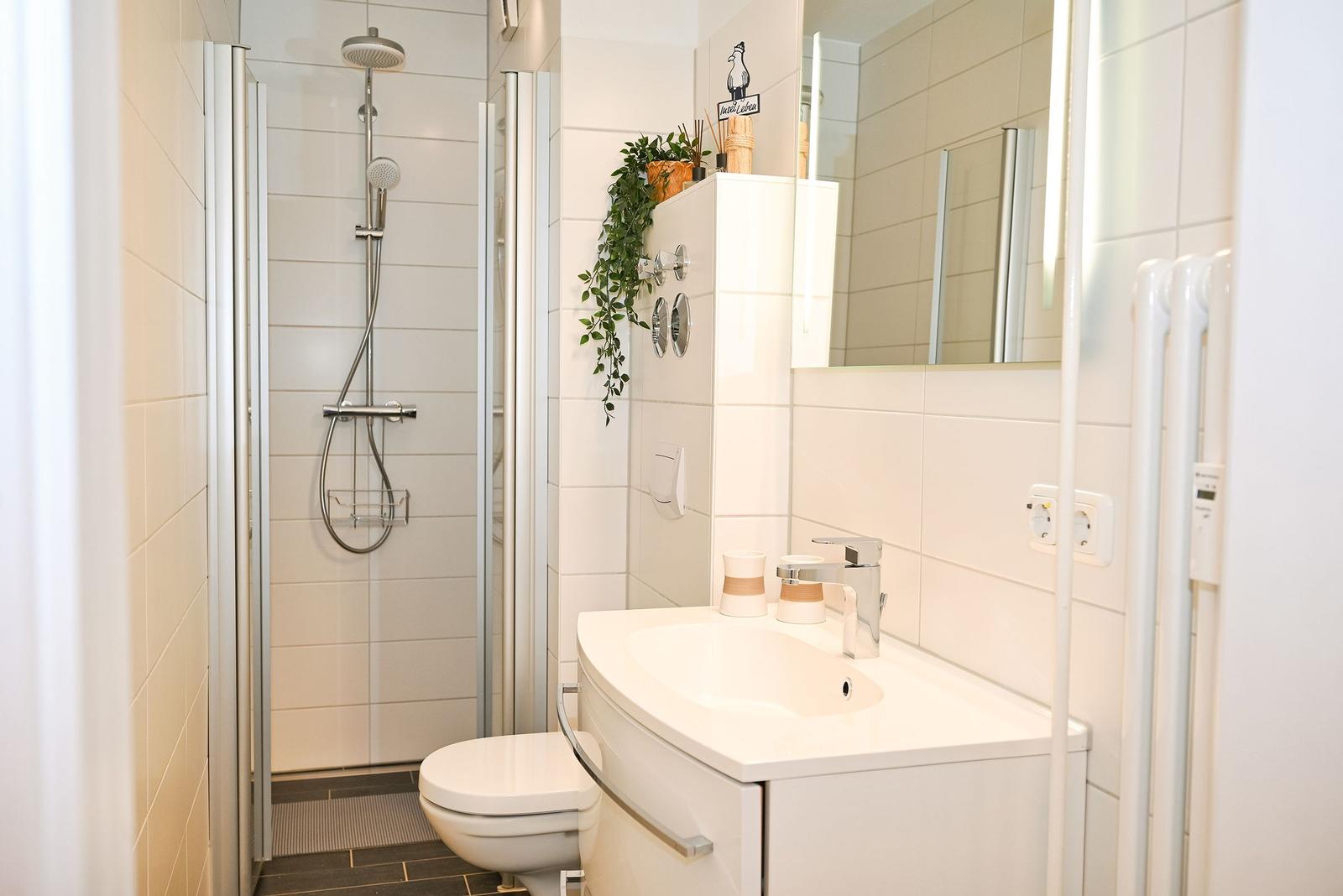 Badezimmer mit Dusche, Waschbecken und Toilette. Weiße Fliesen und moderne Einrichtung.