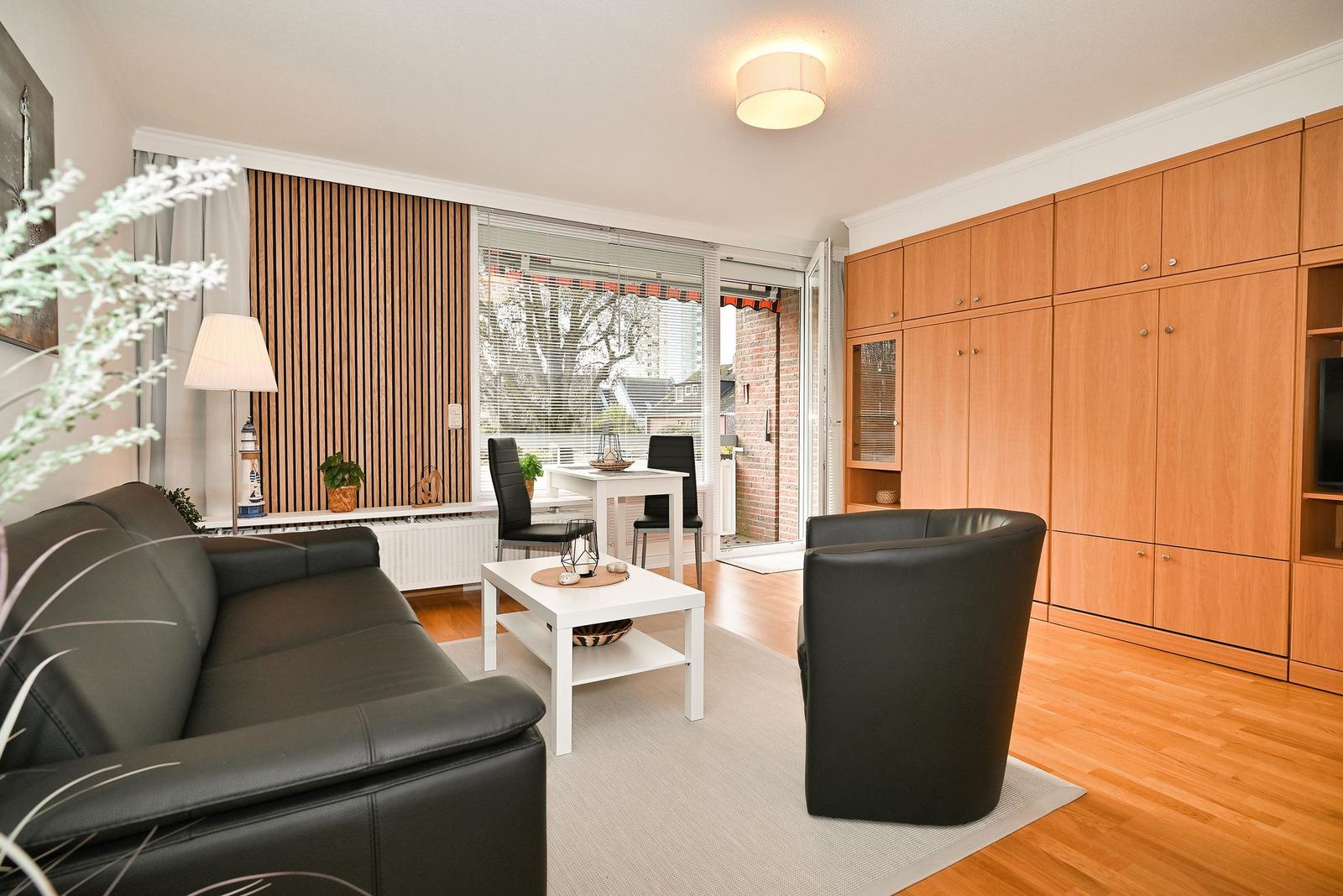 Wohnzimmer mit Sofa, Sessel, Tisch und Holzmöbeln. Durchgang zur Terrasse.