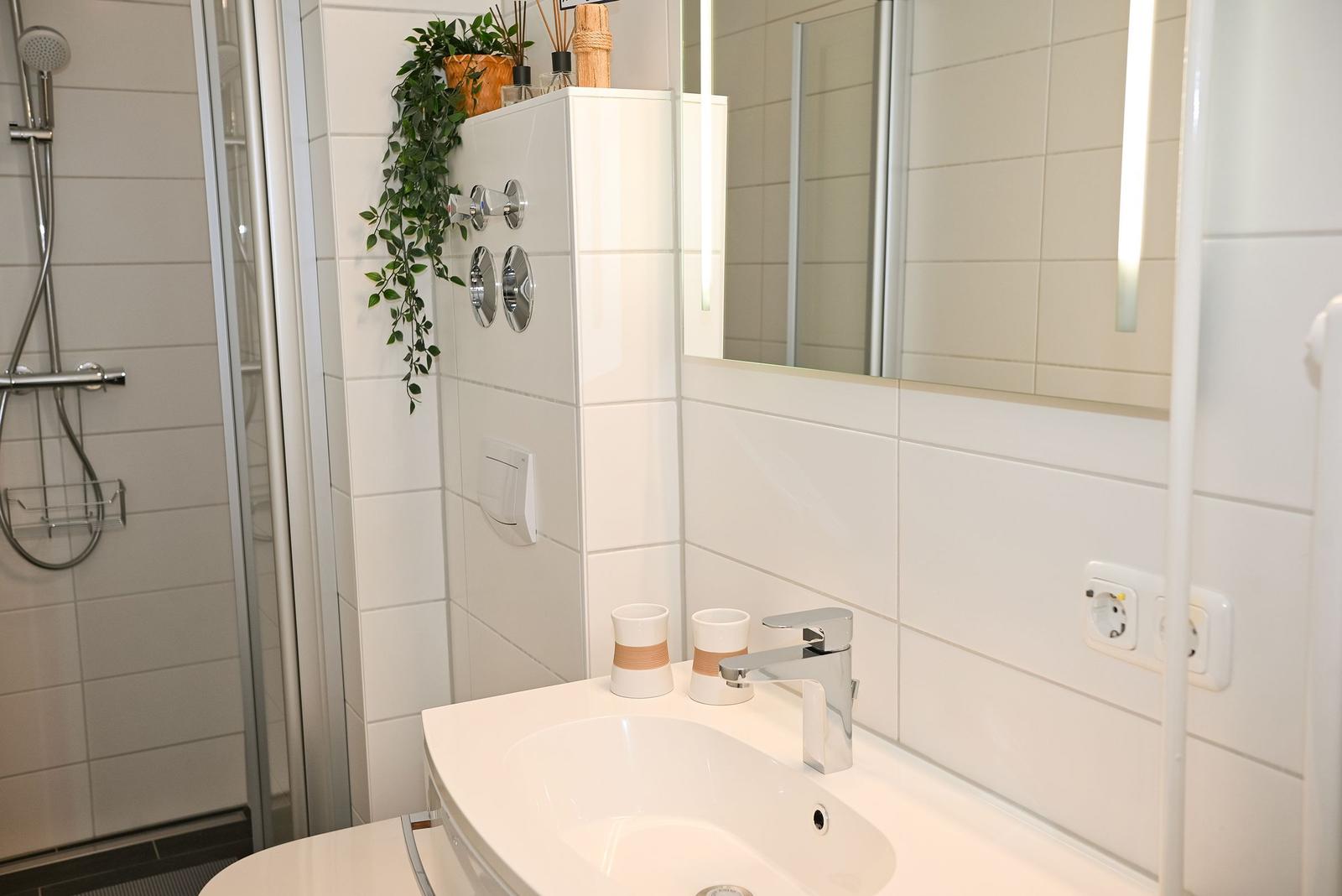 Badezimmer mit Dusche, Waschbecken und Spiegel. Weiße Fliesen und moderne Armaturen.