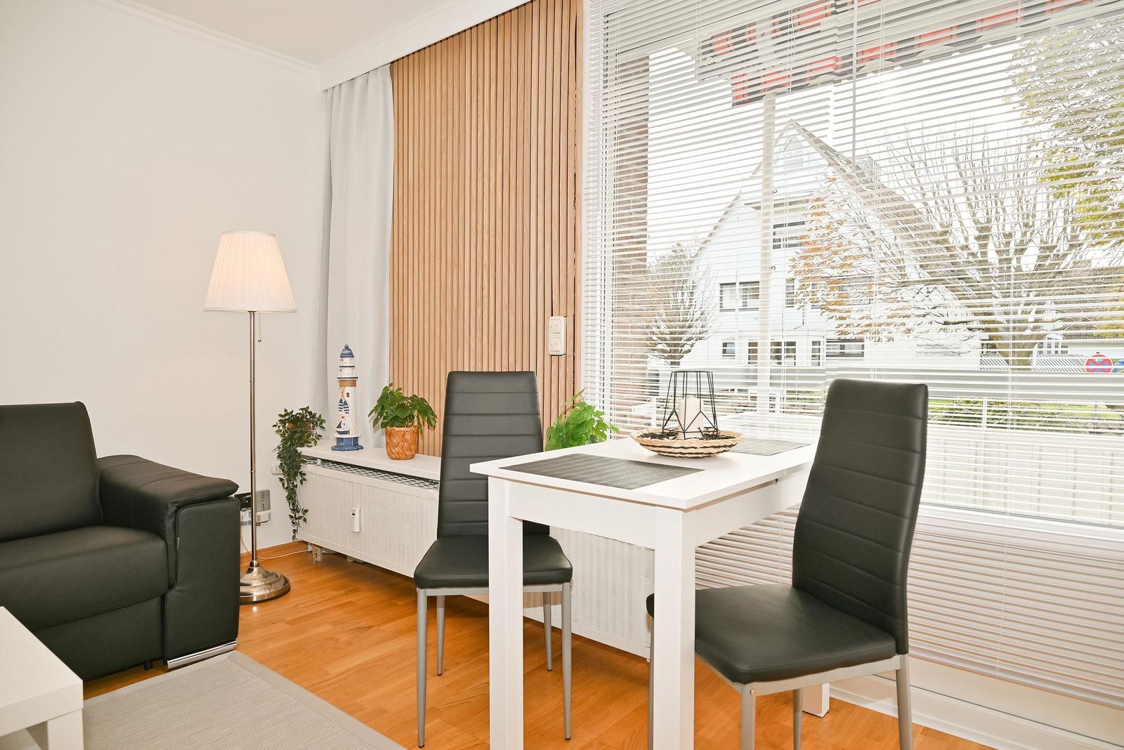 Ein Essbereich mit weißem Tisch, zwei schwarzen Stühlen und Blick auf die Straße.