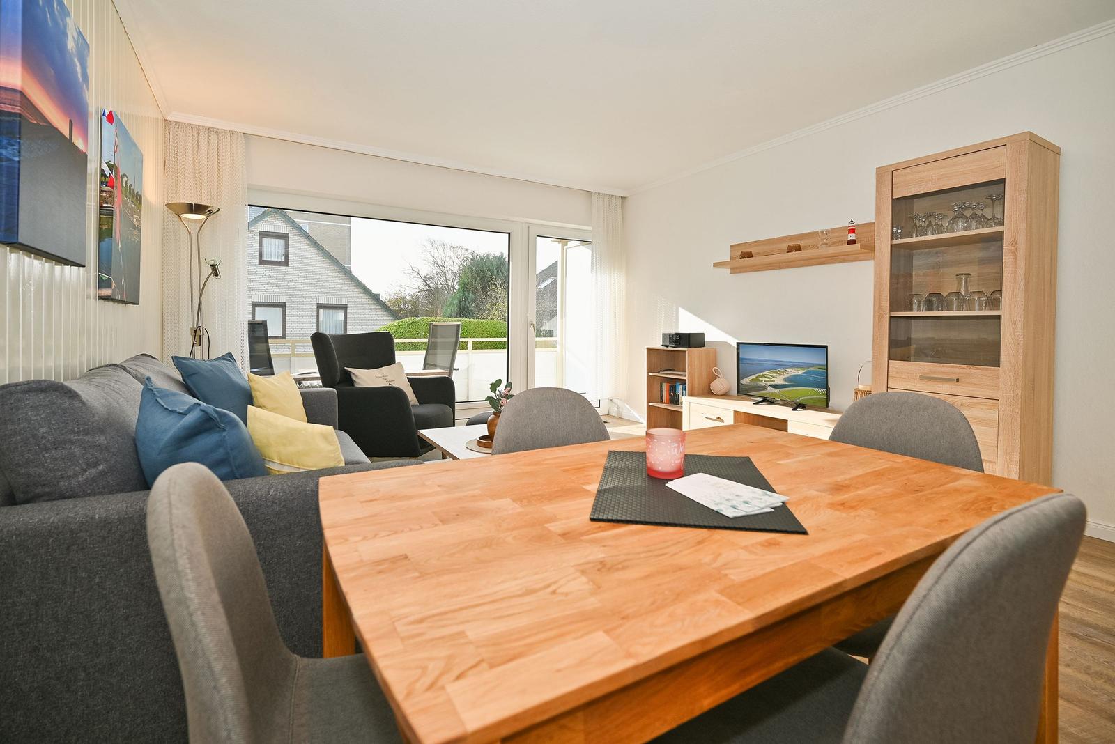 Essbereich mit Holztisch und Stühlen. Wohnbereich mit Sofa, Fernseher und Glasvitrine.