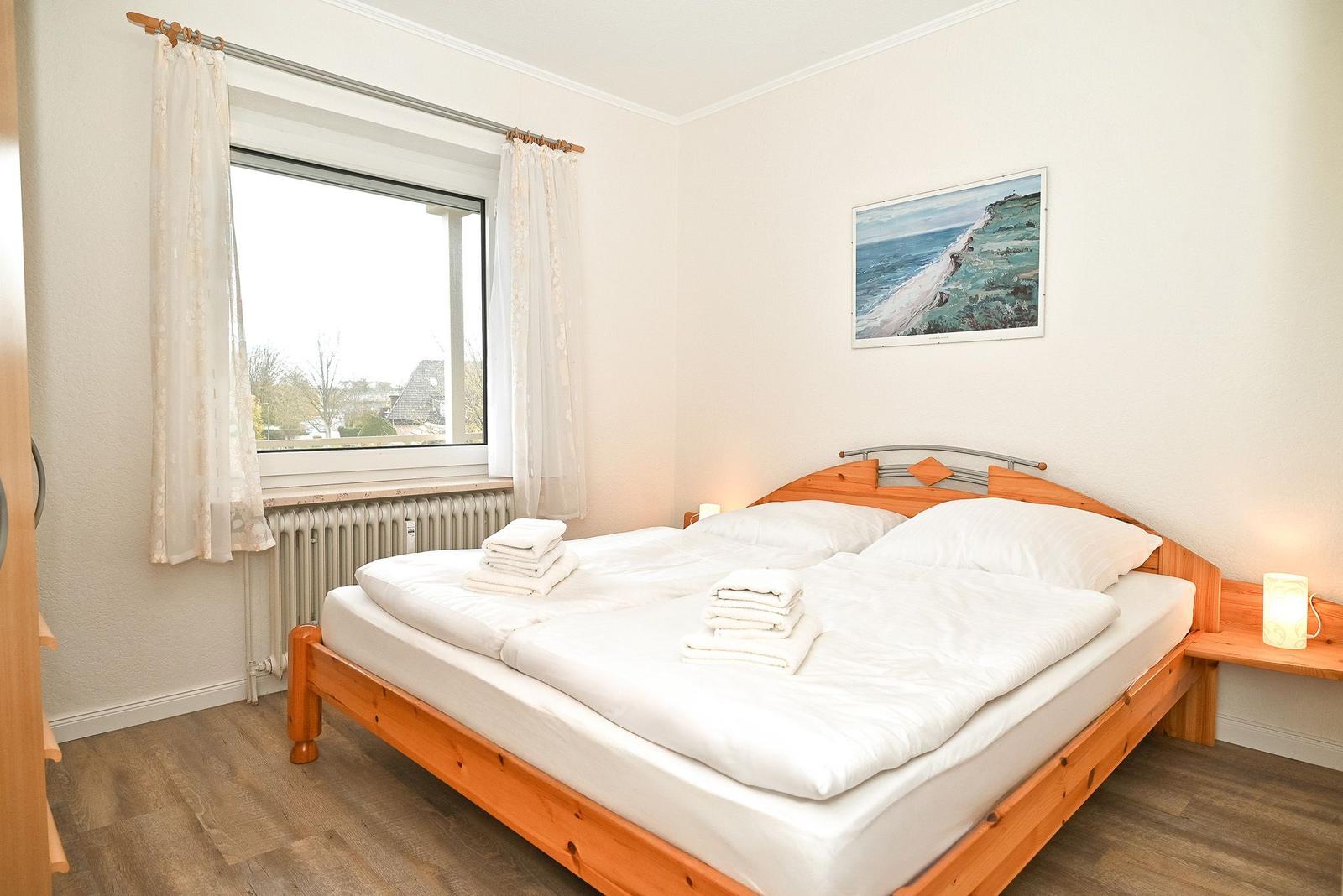 Schlafzimmer mit Doppelbett, Fenster und Wandbild.