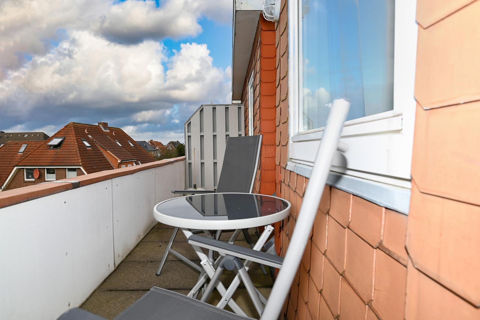 Terrasse mit Tisch und Stühlen, Blick auf Dächer und Himmel.