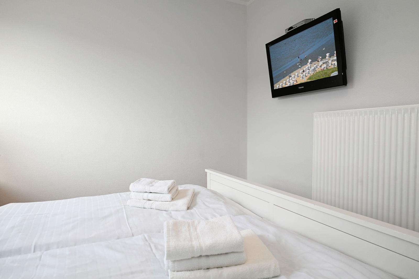 Das Schlafzimmer mit weißem Bett und TV an der Wand.