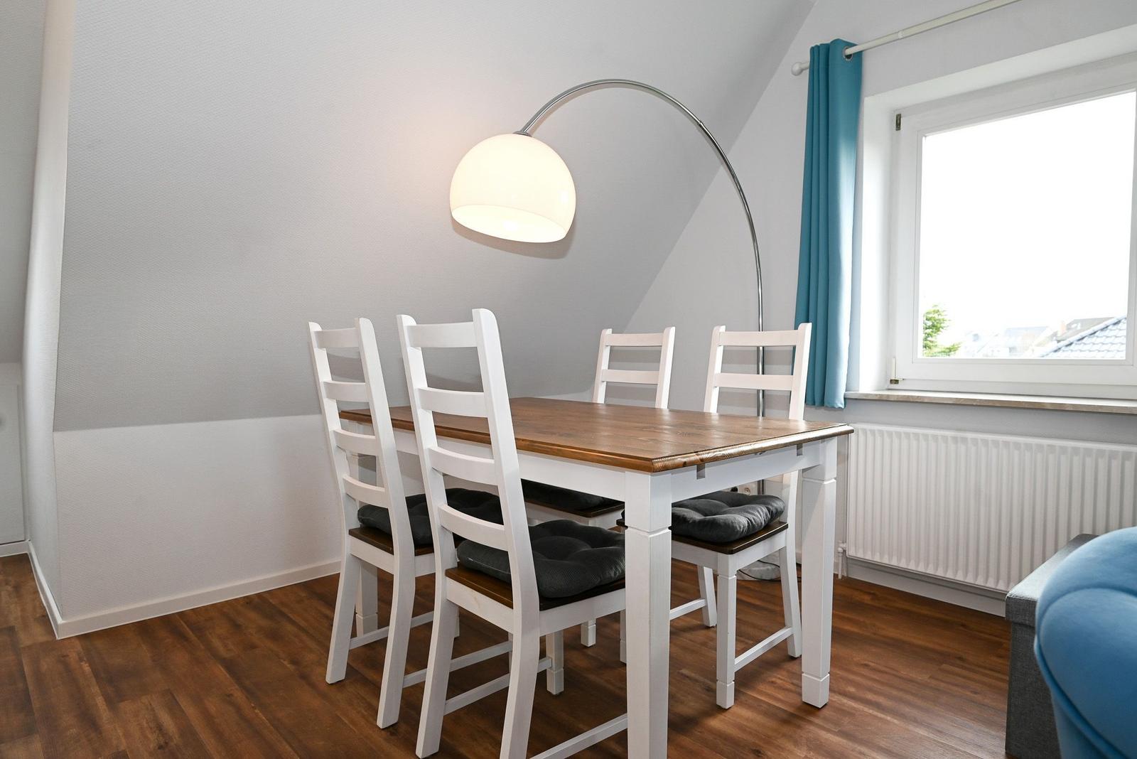 Esstisch mit vier Stühlen, Bogenlampe und Fenster mit blauen Vorhängen.