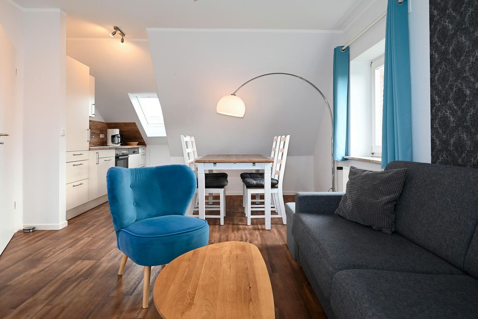 Wohnung mit Essbereich, Sofa, blauer Sessel und Küchenbereich unter Dachschräge.