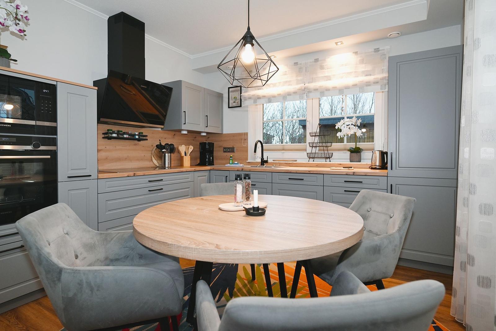 Küche mit Essbereich, Holztisch, grauen Stühlen und Fenster mit Blick nach draußen.