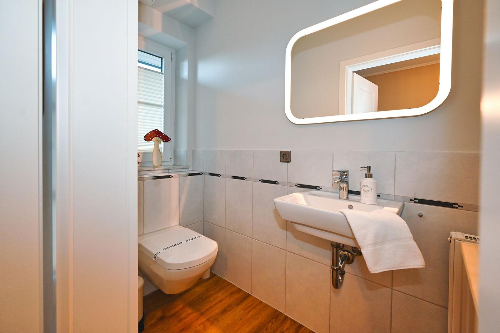 Badezimmer mit Waschbecken, Spiegel, Toilette und Fenster.