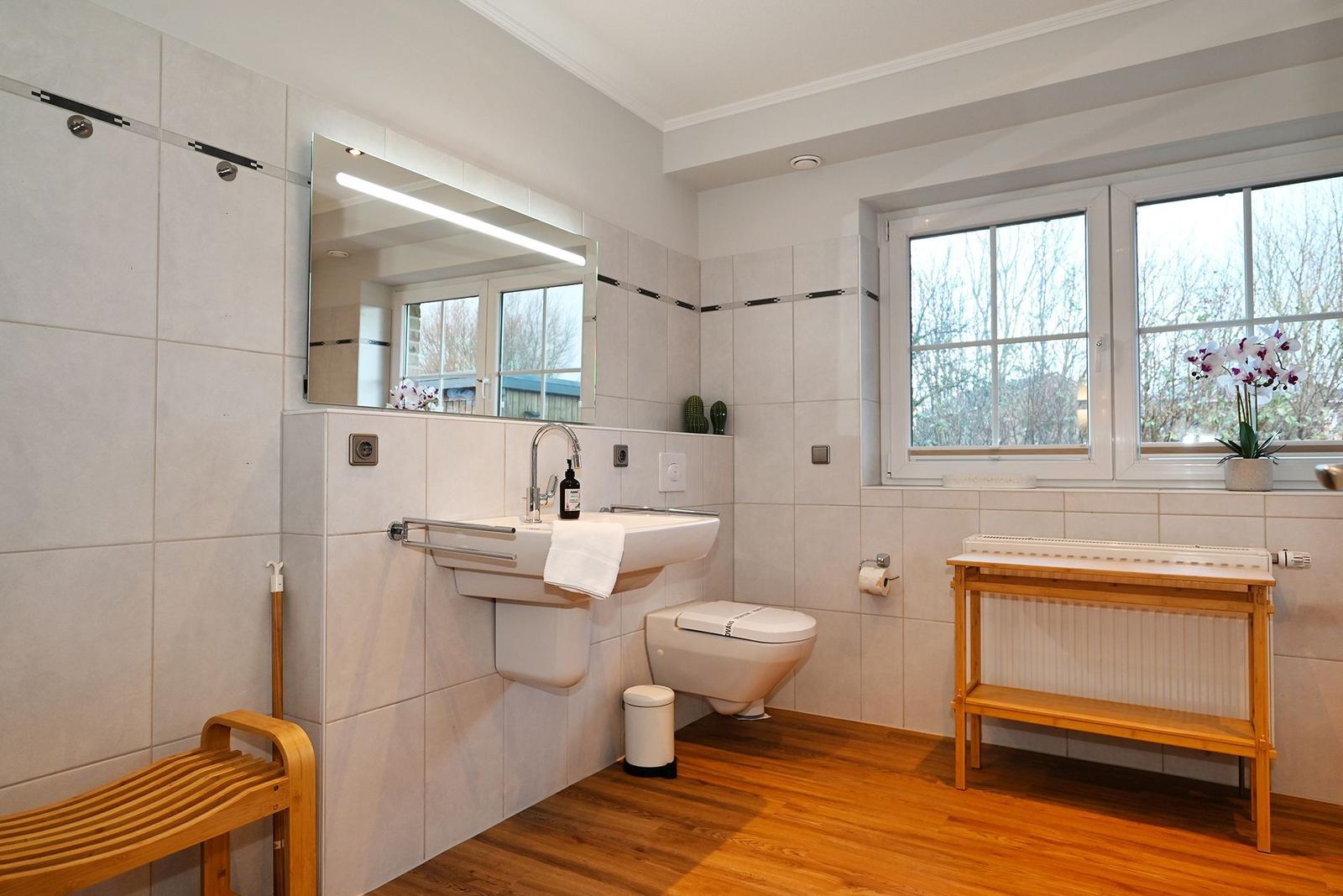 Badezimmer mit Waschbecken, Toilette und Fenster. Holzfußboden und Holzregal.