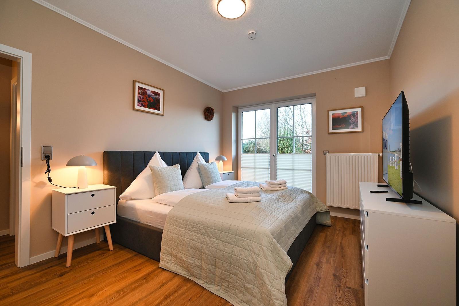 Schlafzimmer mit Bett, Nachttisch, TV und Fenster zur Außenseite.