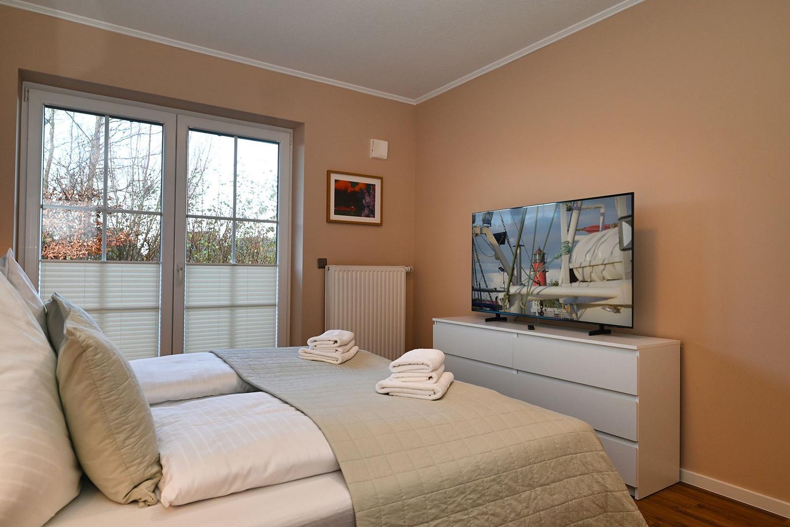 Schlafzimmer mit Doppelbett, TV und Fenster zur Außenseite.