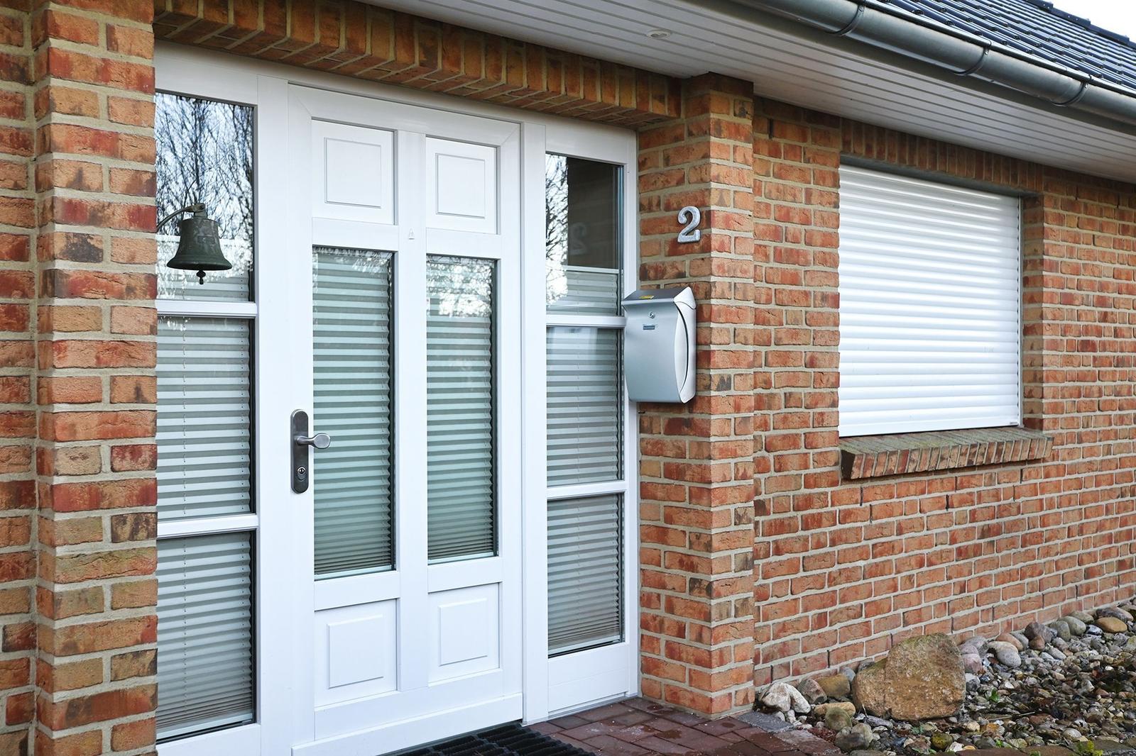 Haus mit weißer Haustür, Briefkasten und Ziffer 2 an der Backsteinfassade.