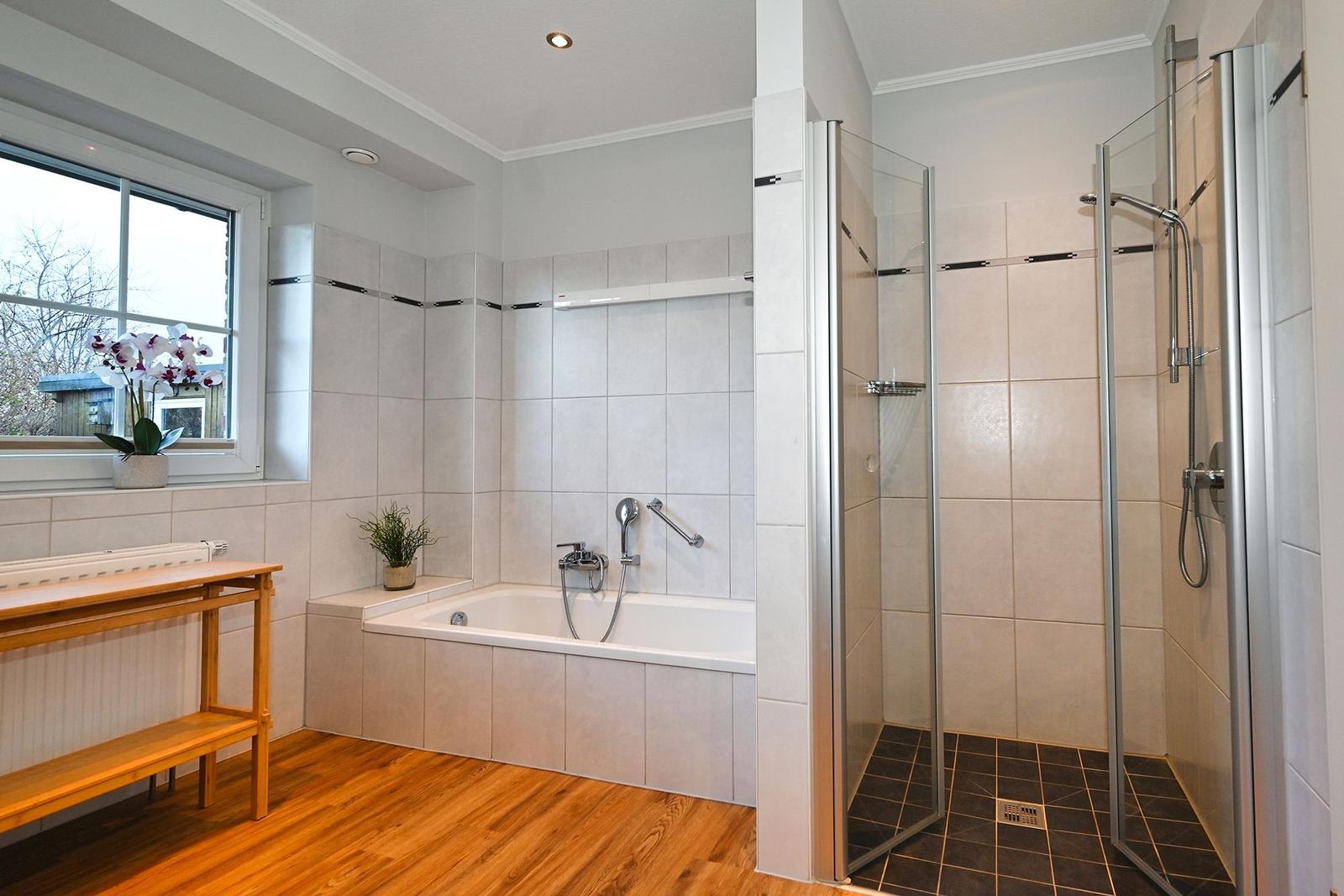 Bad mit Badewanne, Dusche und Holzboden. Fenster mit Pflanze.