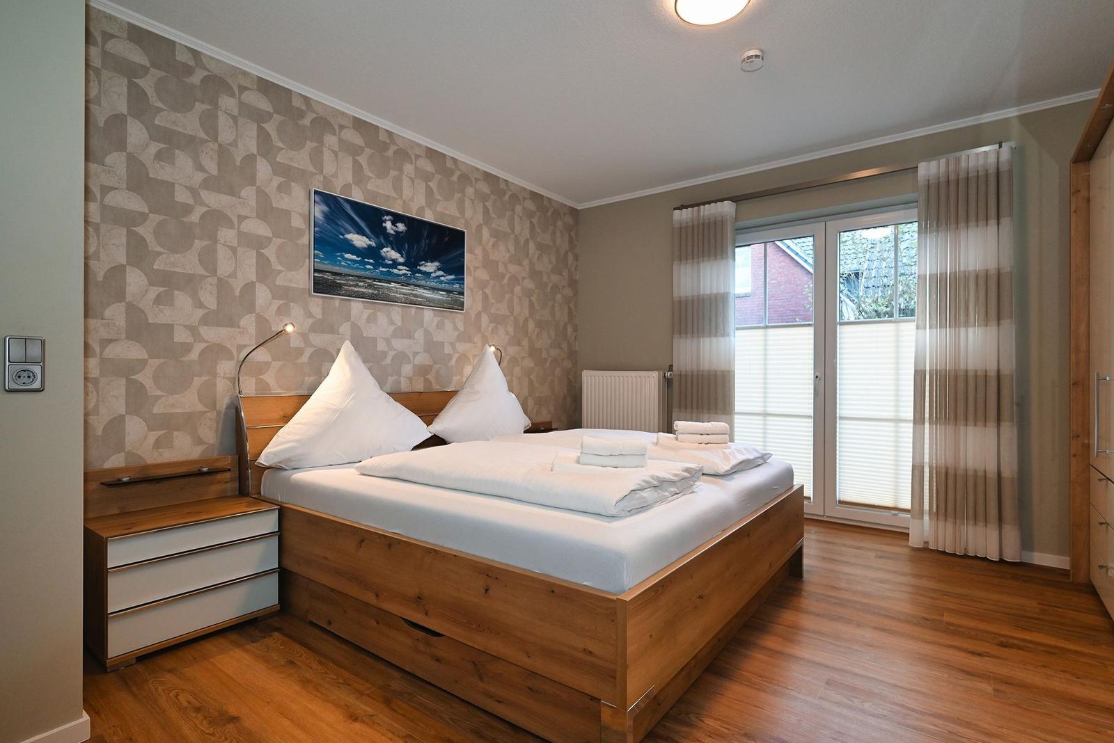 Schlafzimmer mit Holzbett, Wandbild und Schiebetür zum Balkon.