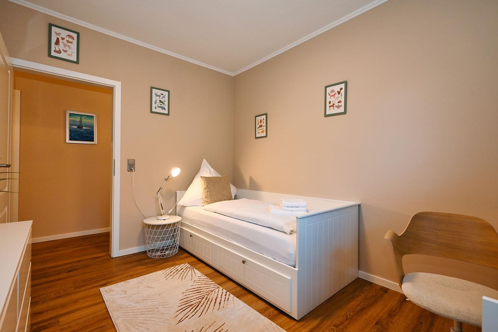 Schlafzimmer mit Bett, Stuhl und Wandbildern.