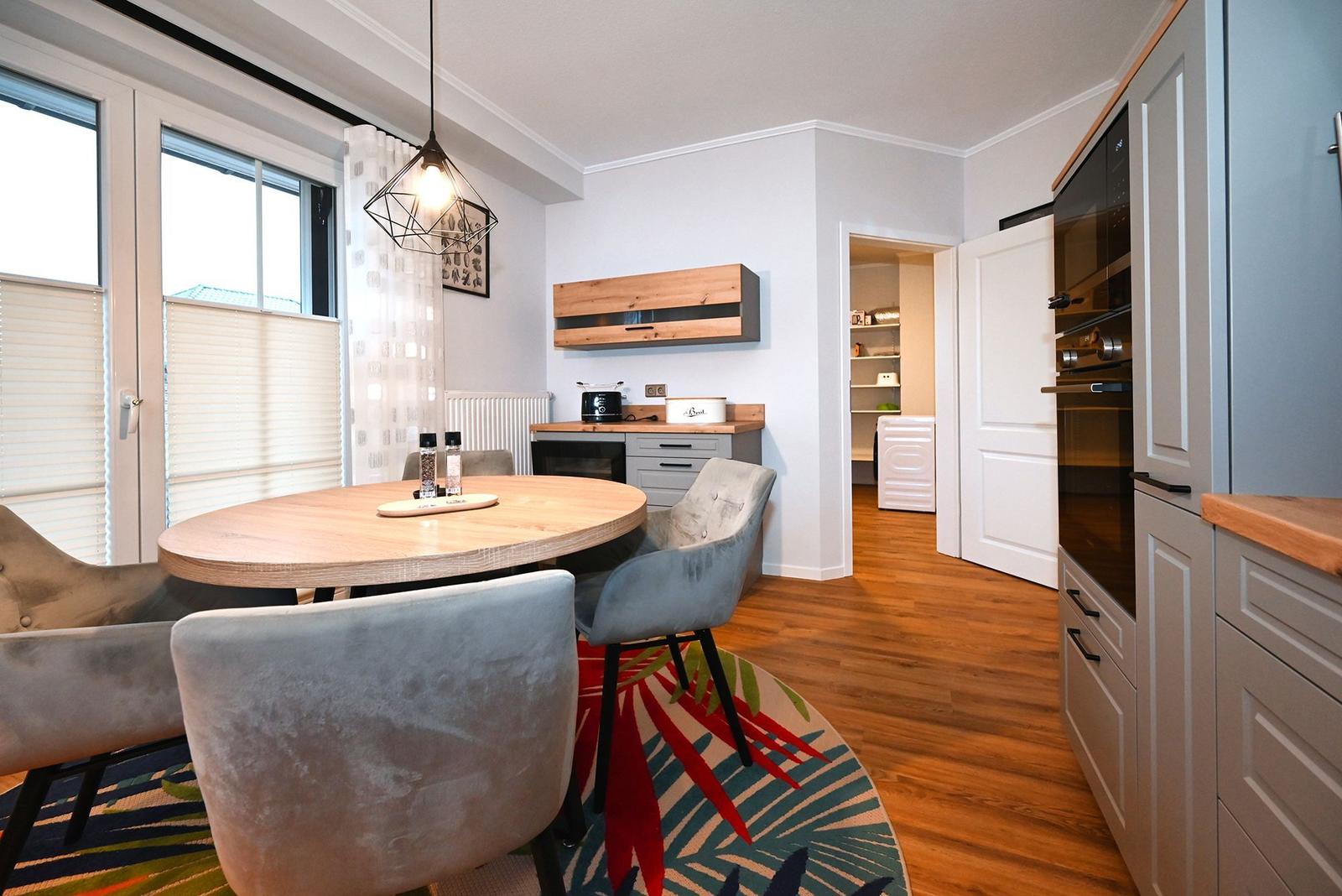 Essbereich mit runder Tisch, Stühlen und Küchenzeile. Holzfußboden und Fenster mit Jalousien.