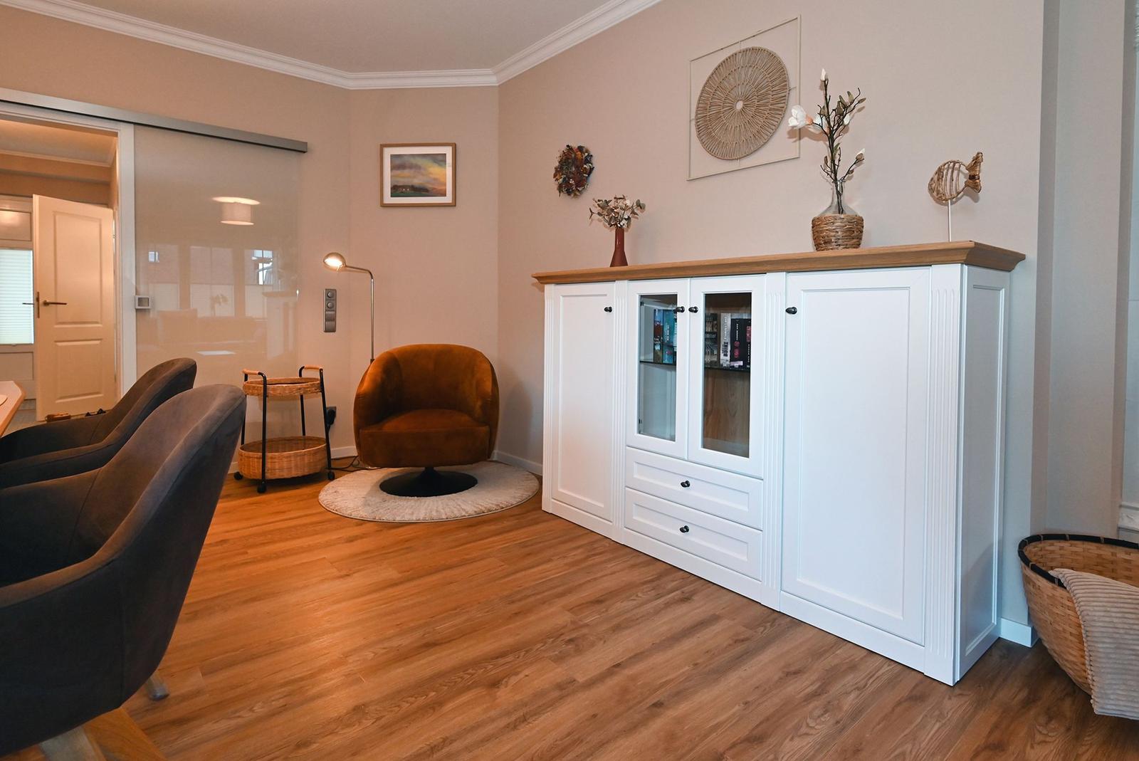 Wohnbereich mit weißen Schränken, braunem Sessel und Holzboden.