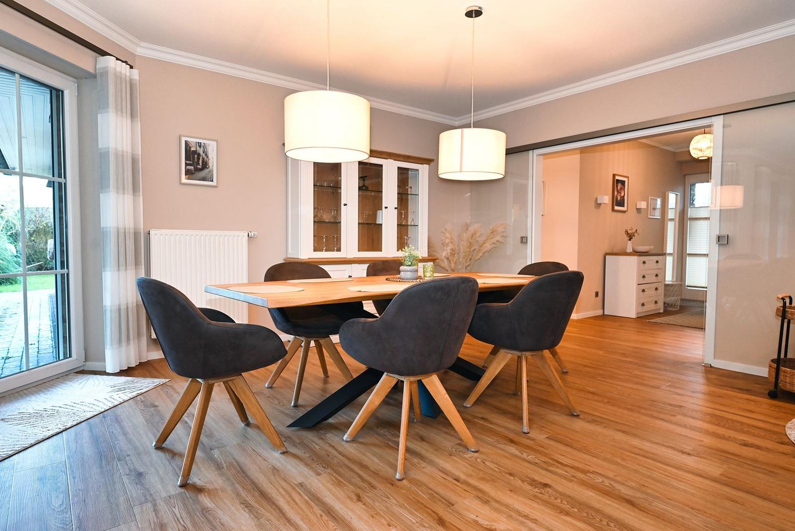 Esszimmer mit Holztisch, dunklen Stühlen und zwei Hängelampen. Durchgang zur Schlafzimmerseite.