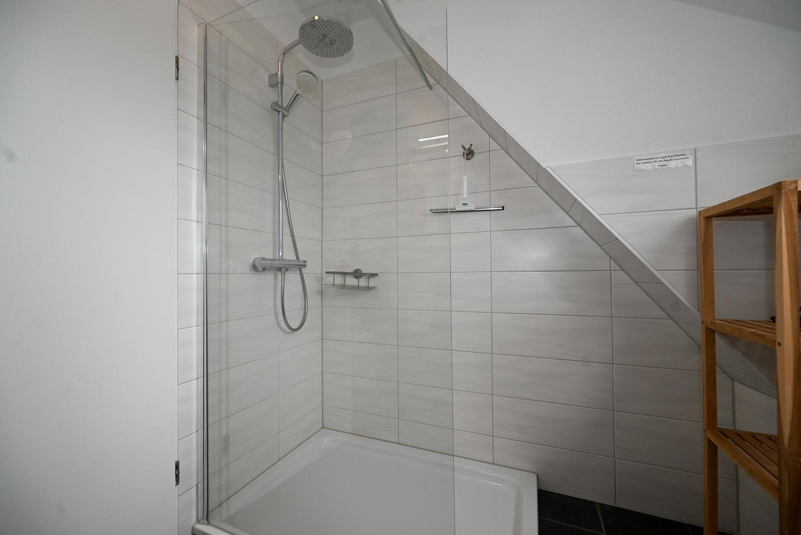 Dusche mit Glaswand, Duschbrause und Holzregal an der Wand