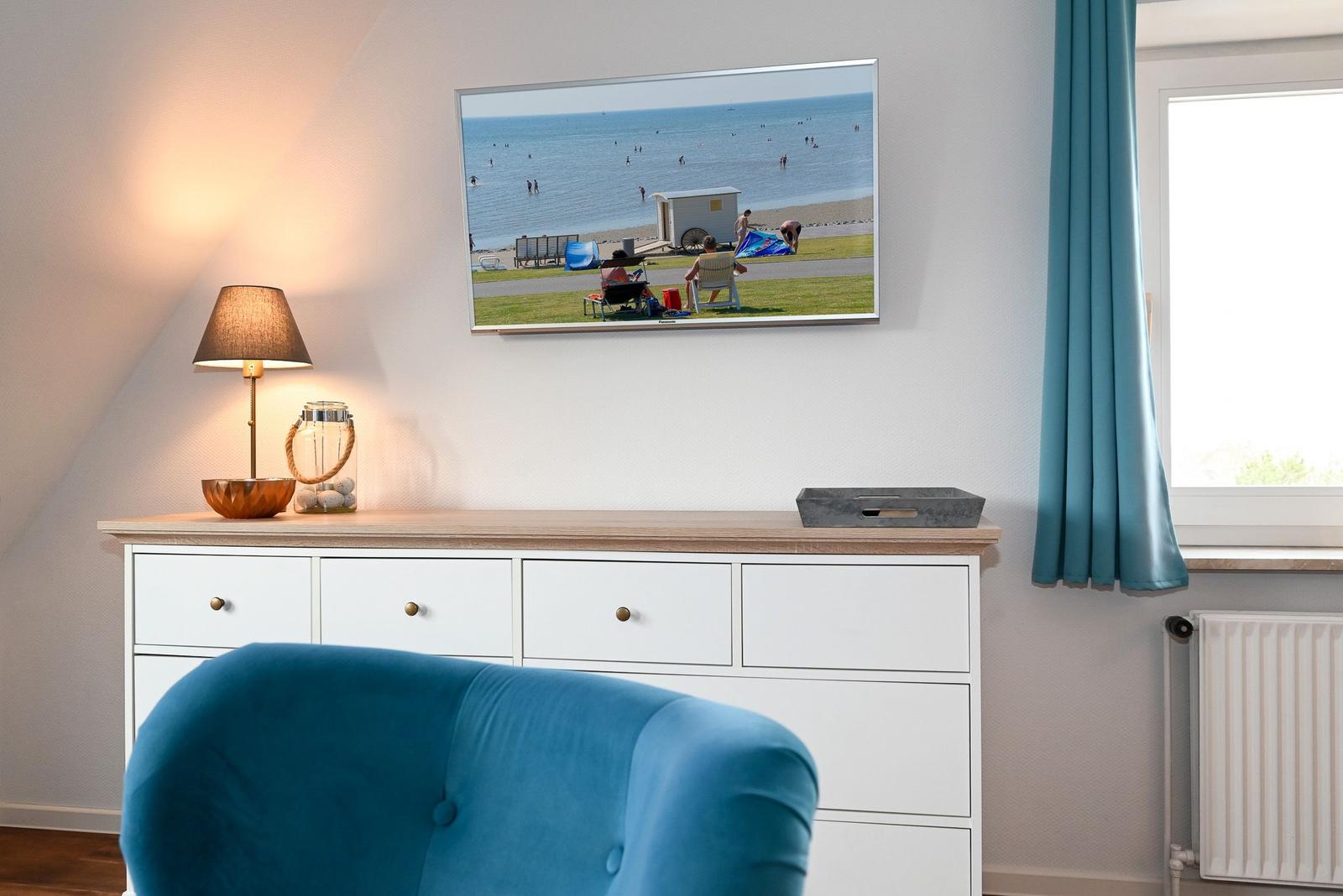 Ein Raum mit blauem Sessel, Schrank und Wandbild eines Strandes.