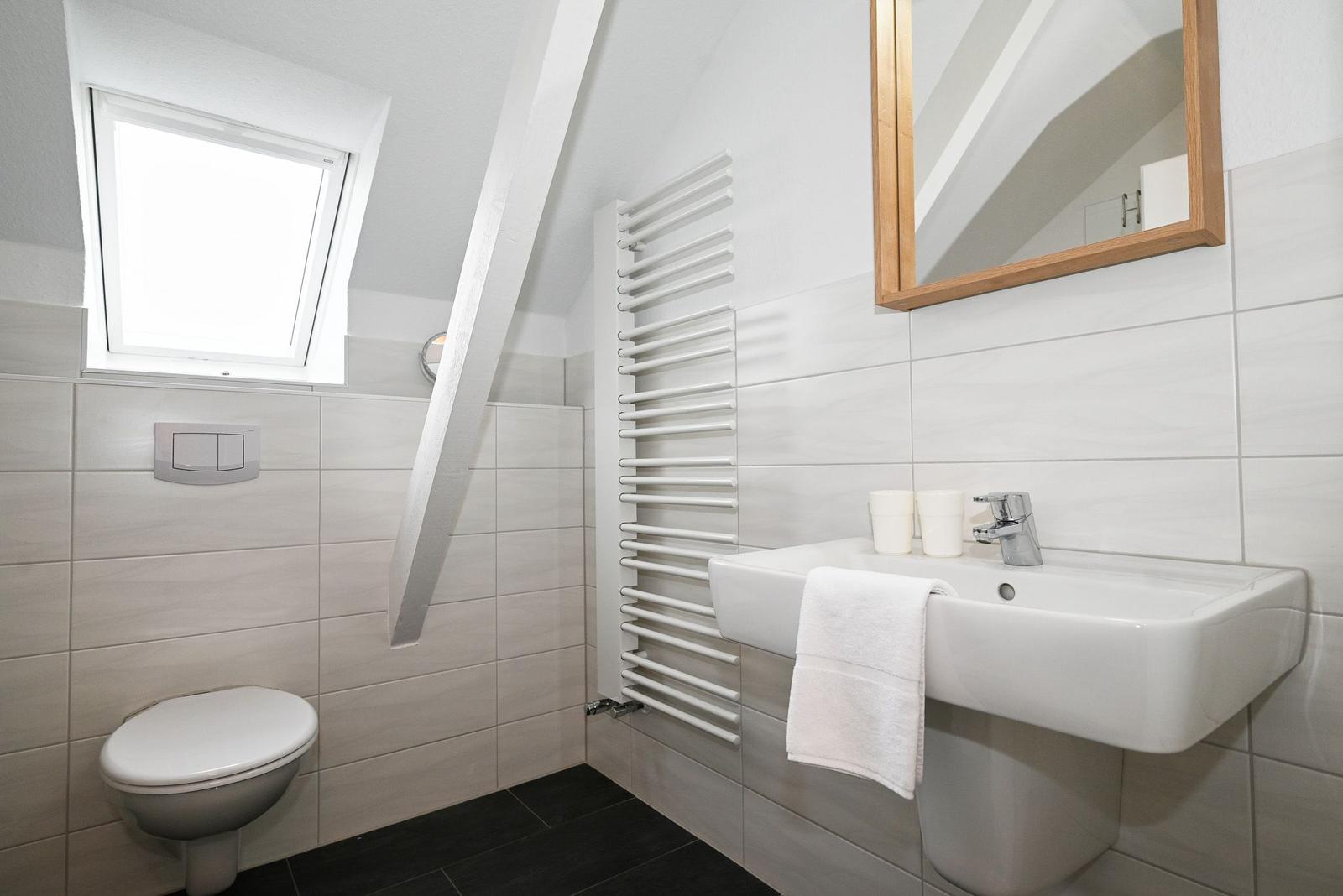 Badezimmer mit Toilette, Waschbecken und Dachfenster. Weiße Fliesen und Holzspiegel.