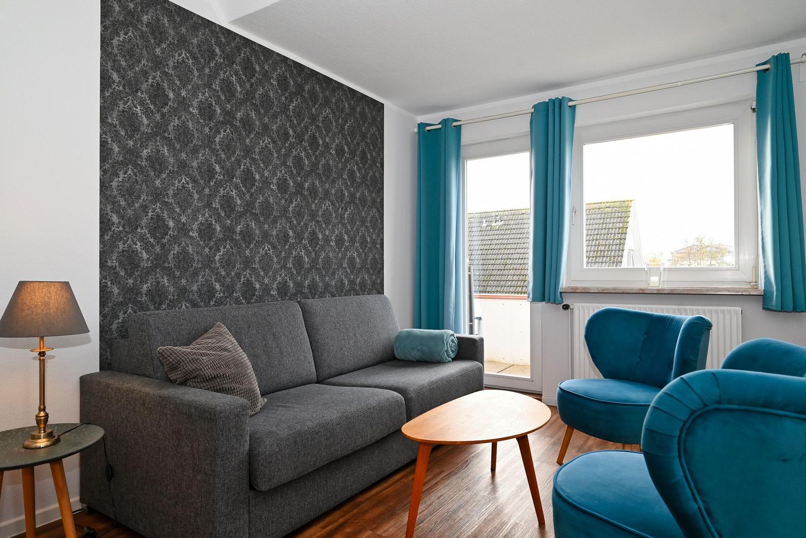 Wohnzimmer mit grauem Sofa, blauen Sesseln und Holztisch. Fenster mit blauen Vorhängen.