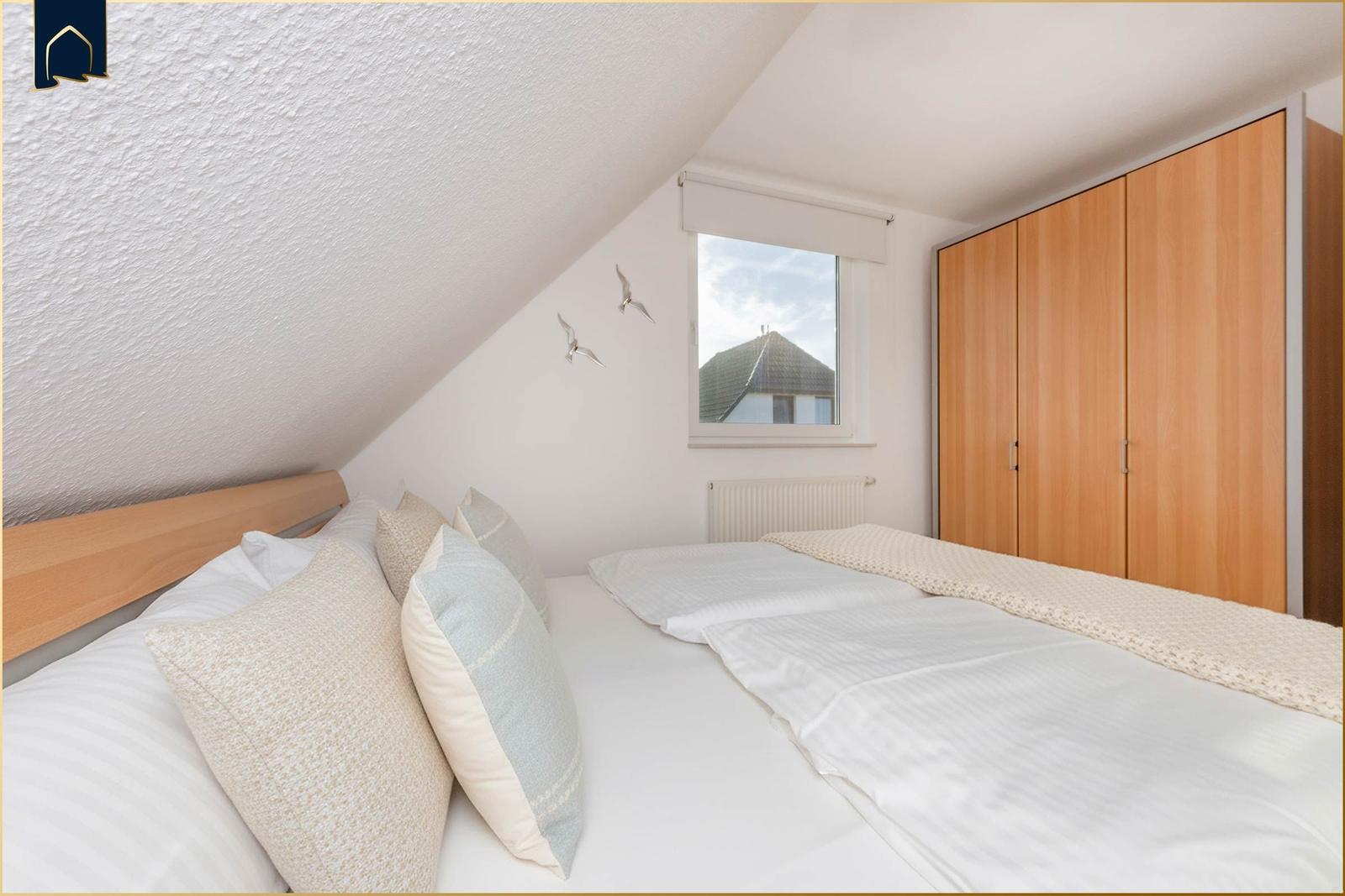 Schlafzimmer mit Dachschräge, Bett, Kleiderschrank und Fenster mit Blick auf Dach.