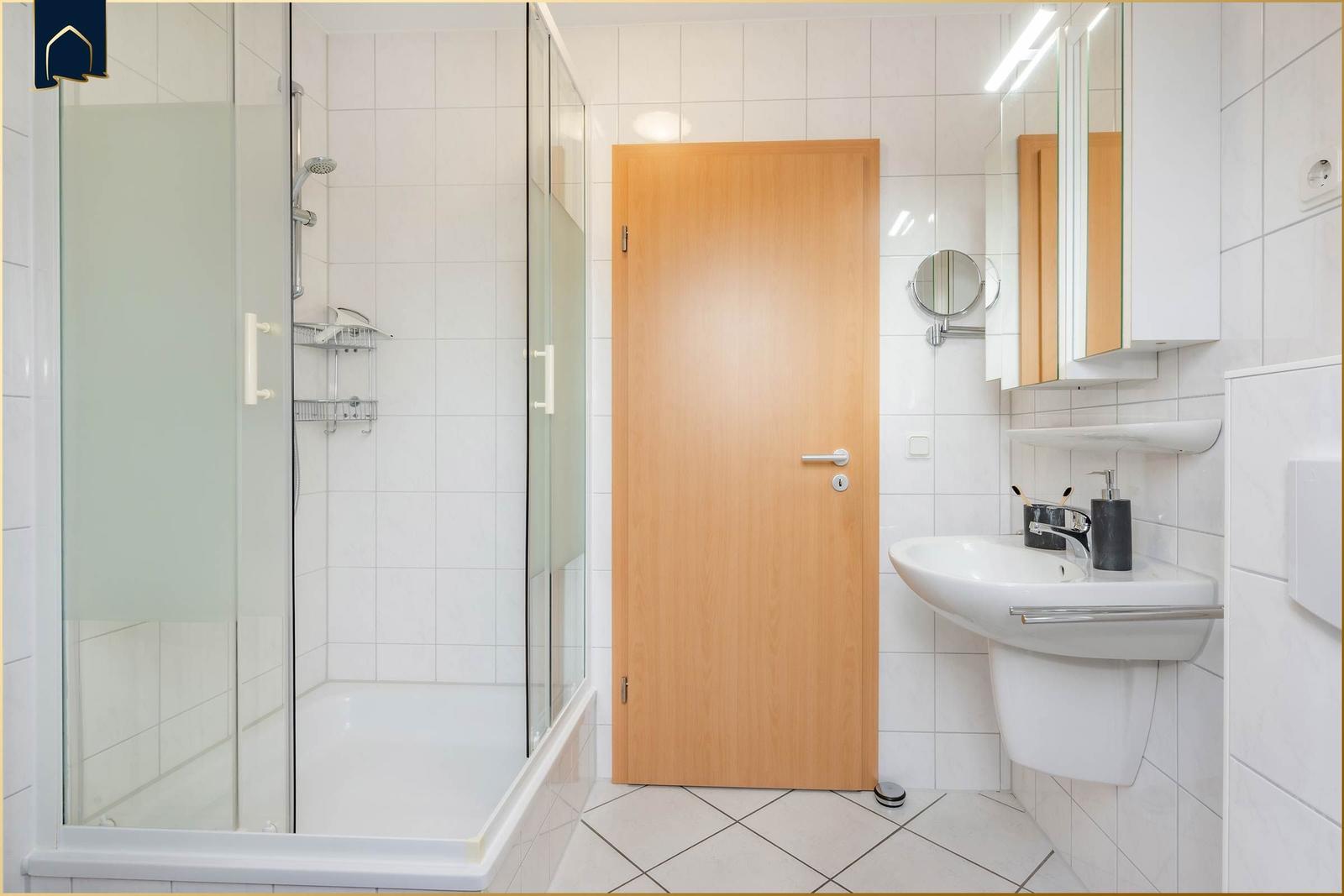 Badezimmer mit Dusche, Waschbecken und Spiegel.