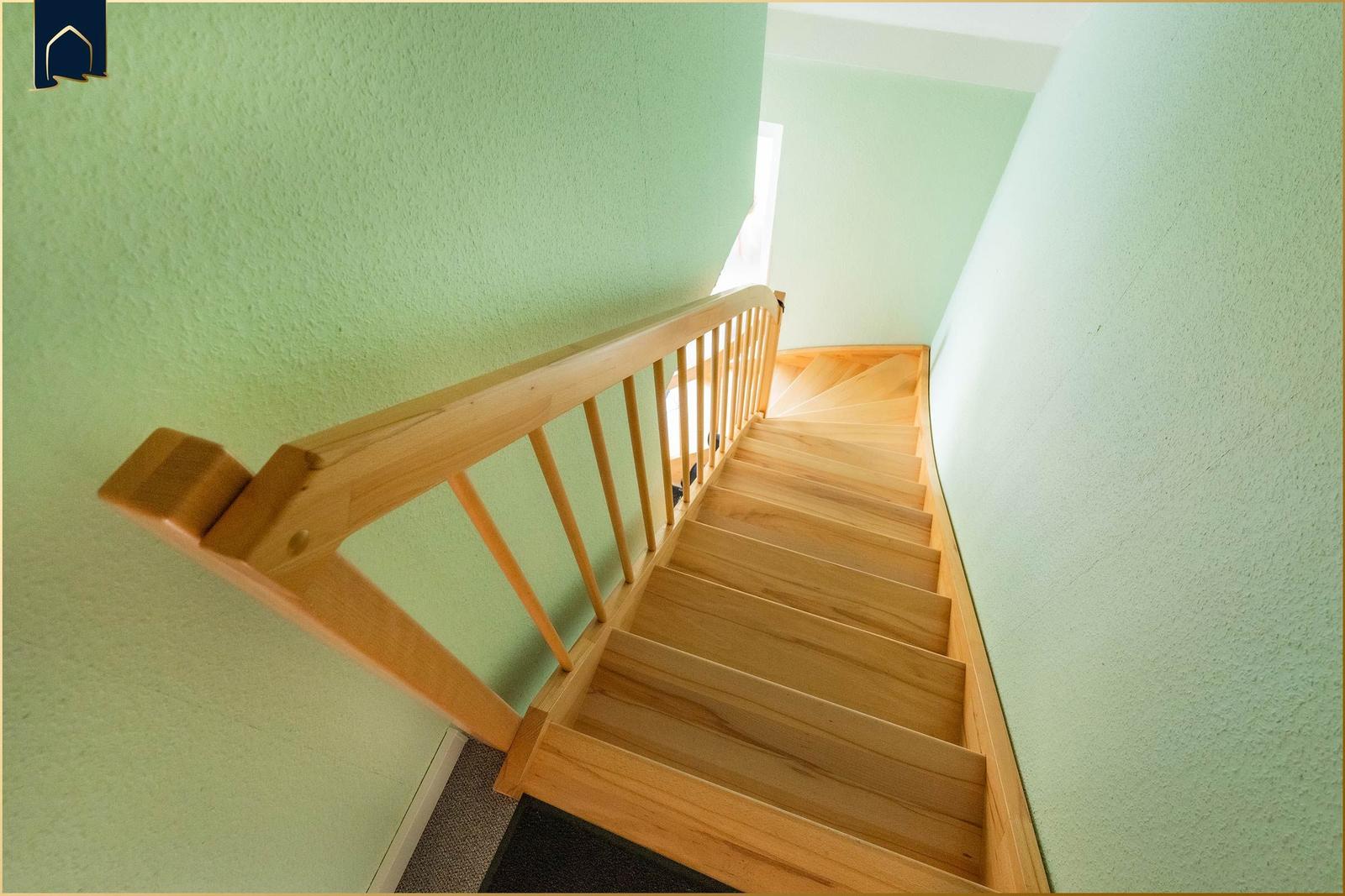 Holzgetreppe mit Geländer führt nach oben. Wände sind hellgrün gestrichen.
