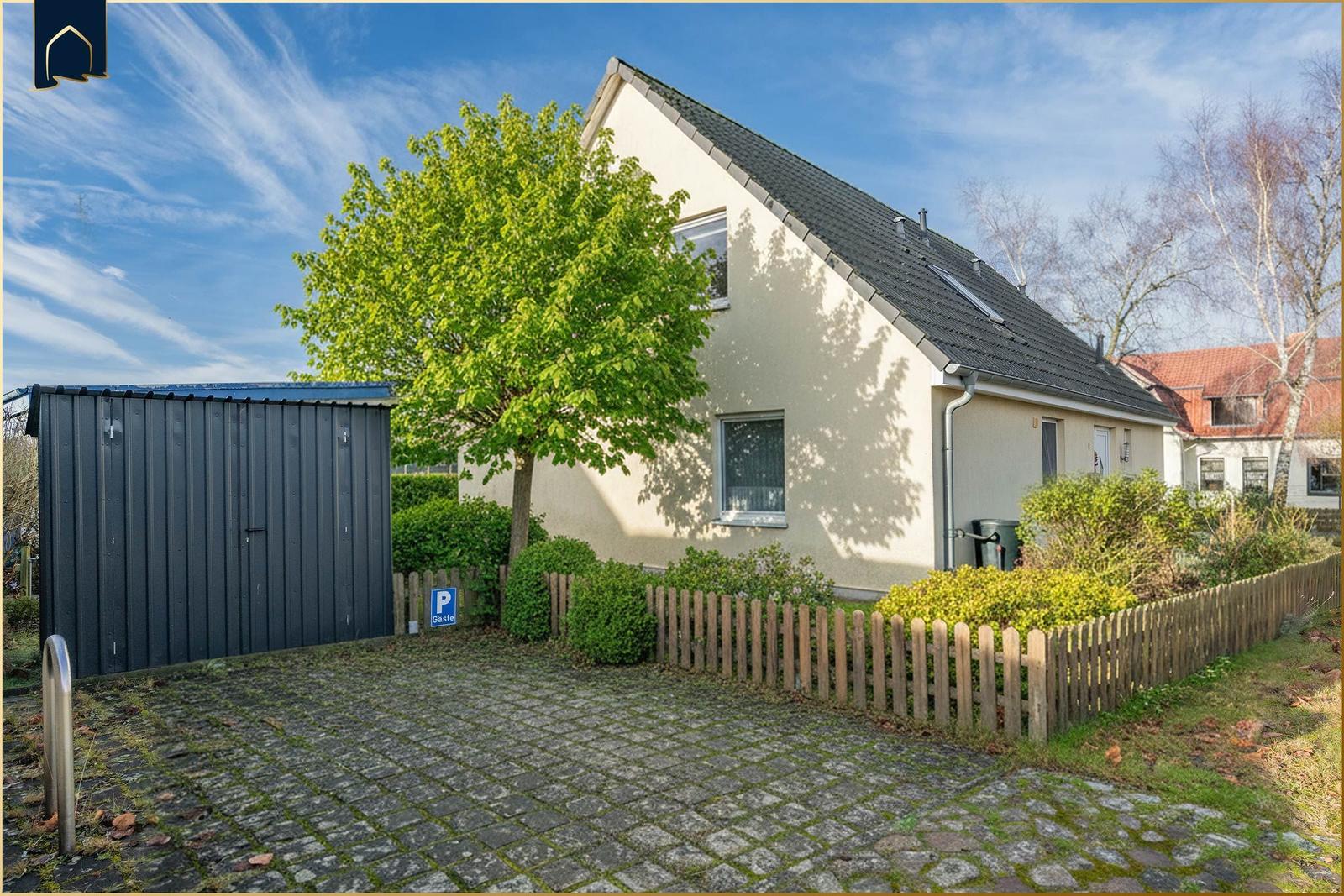 Ein Haus mit Garten, Holzzaun und Steinpflaster. Links steht ein Metallschuppen.