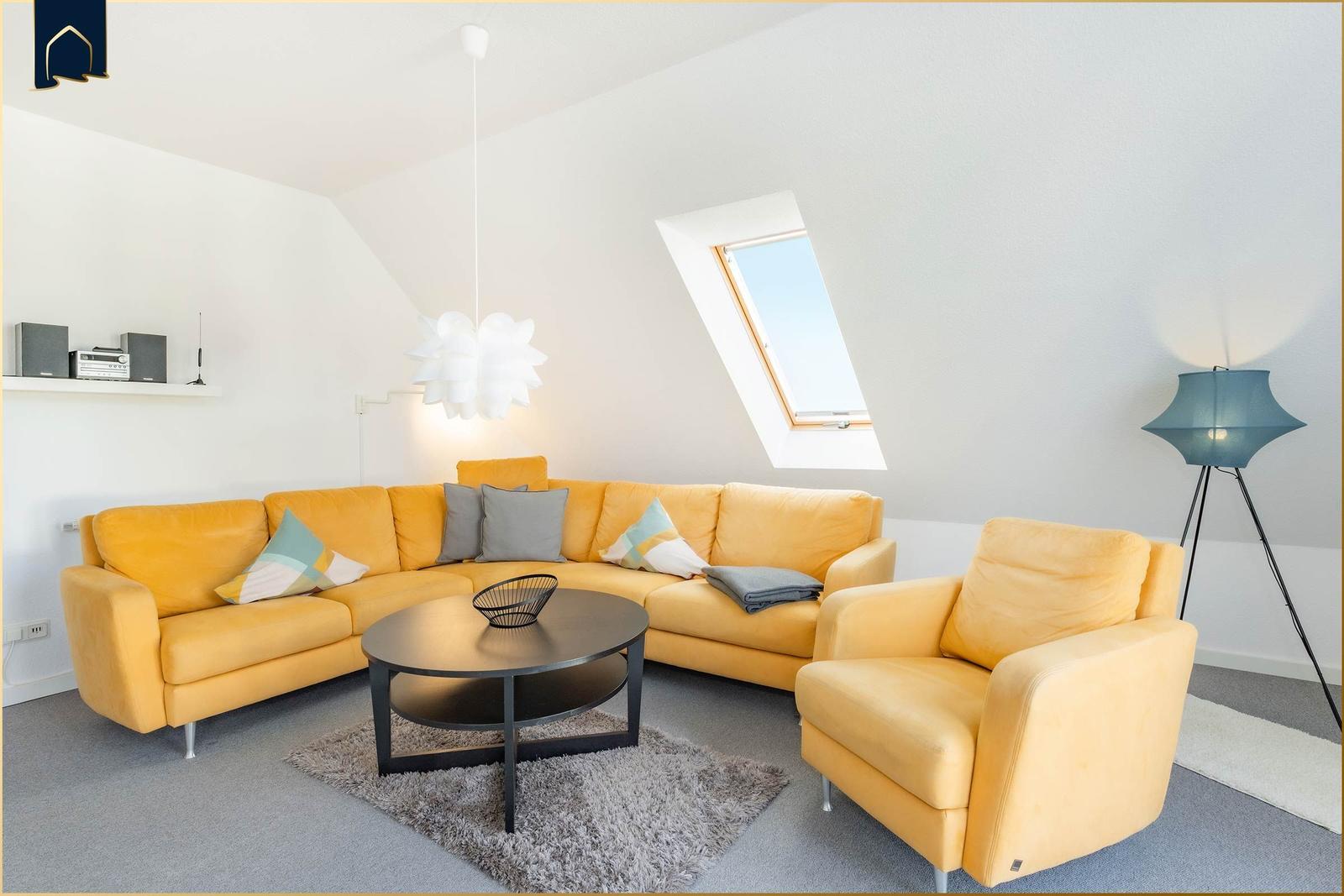 Ein Wohnzimmer mit gelbem Sofa, runden Tisch und Dachfenster.
