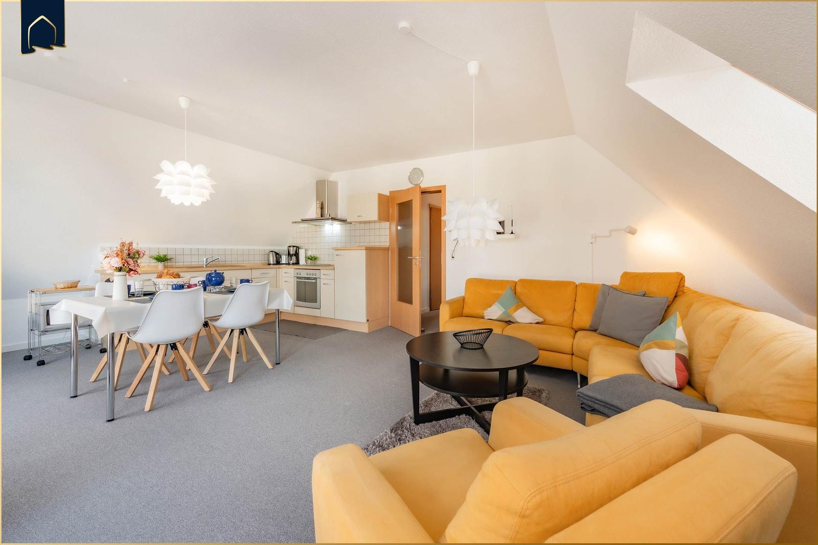 Wohn- und Essbereich mit Küche unter Dachschrägen. Gelber Sofa, Esstisch mit Stühlen.