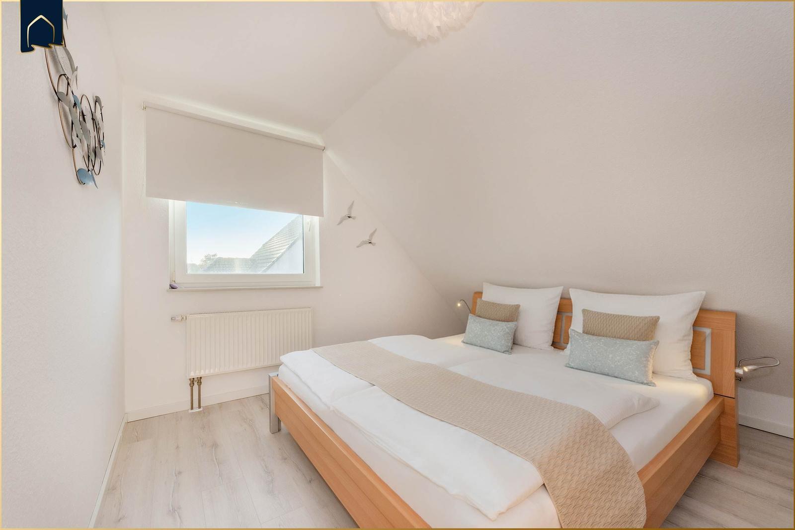 Schlafzimmer mit Dachschrägen, Bett, Fenster und Heizung.
