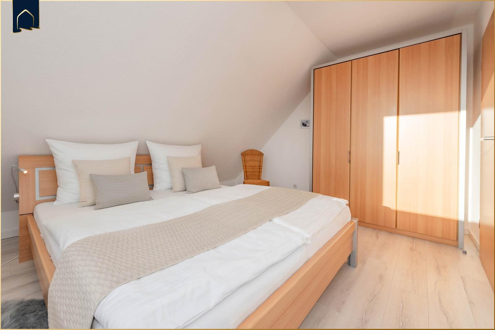 Schlafzimmer mit Doppelbett, Kleiderschrank und Wickerstuhl unter Dachschrägen.
