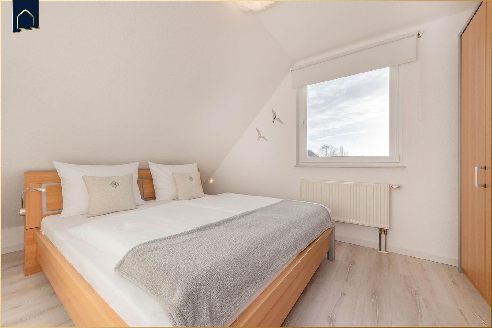 Schlafzimmer mit Dachschräge, Bett, Fenster und Kleiderschrank.