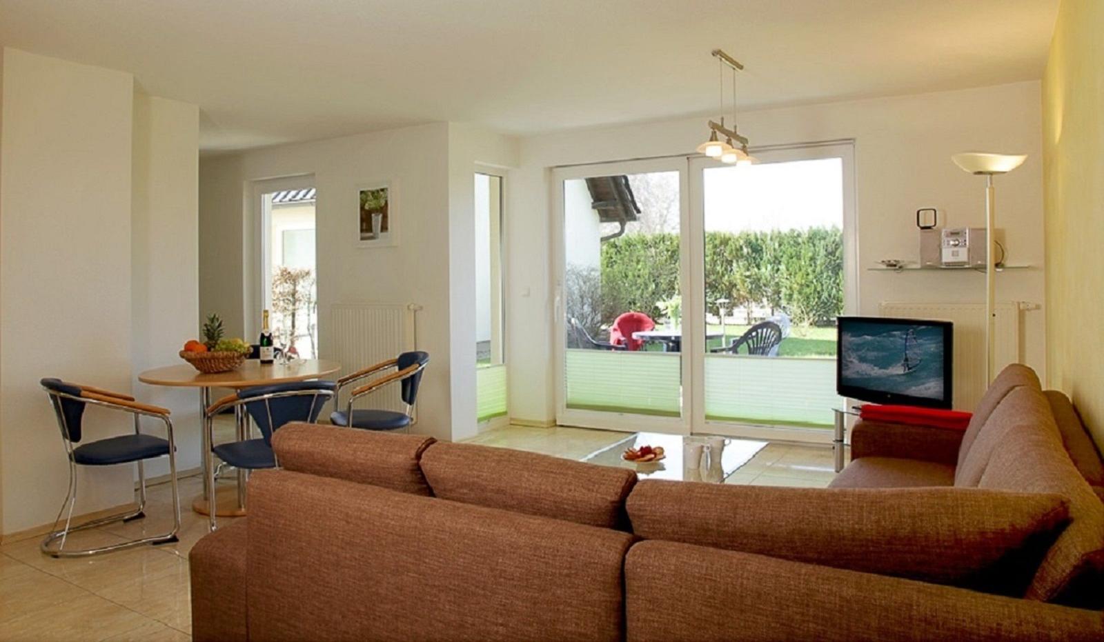 Wohnbereich mit Sofa, Fernseher und Terrasse mit Gartenblick.